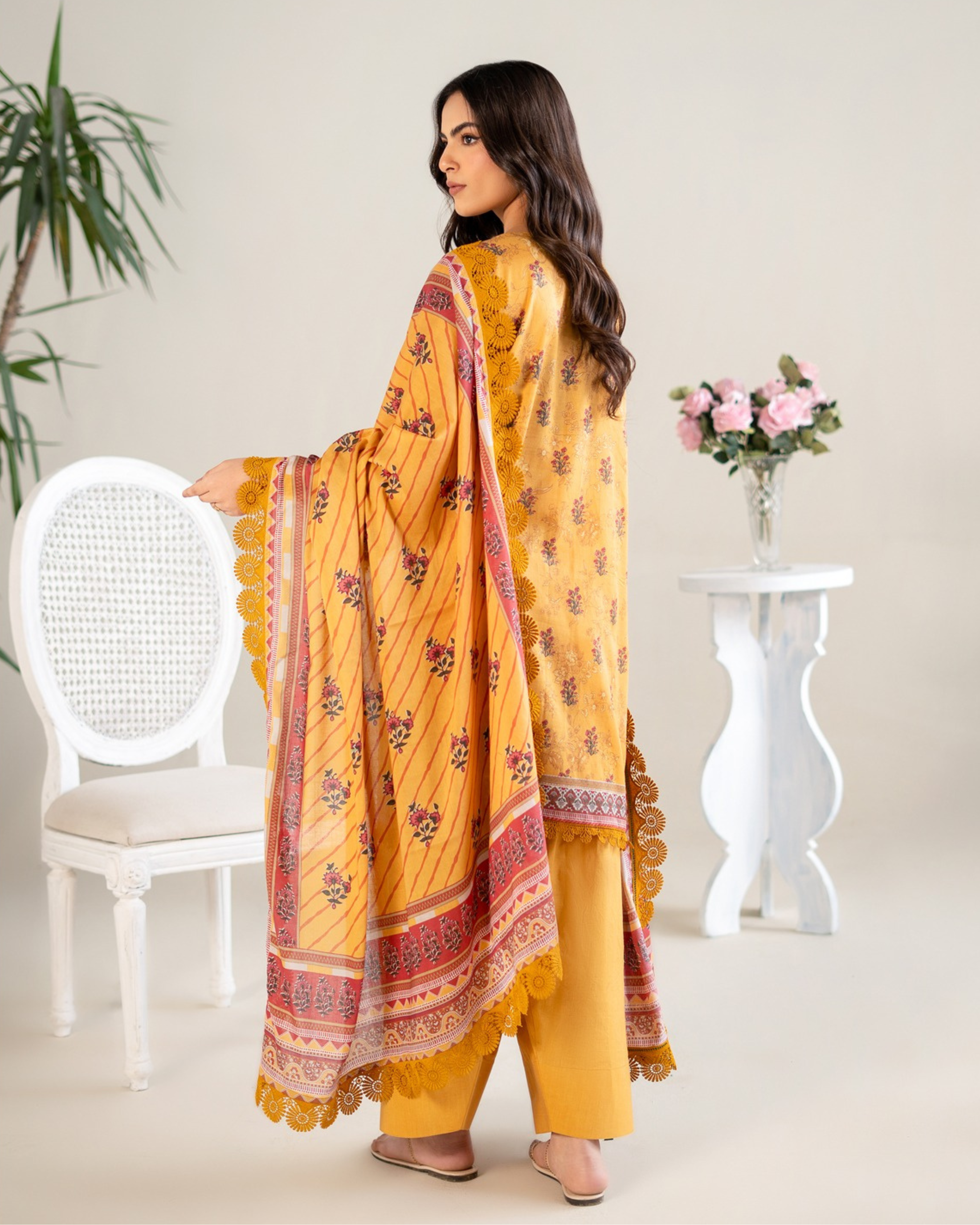 Woman in a yellow traditional outfit with a floral pattern in a minimalistic setting.