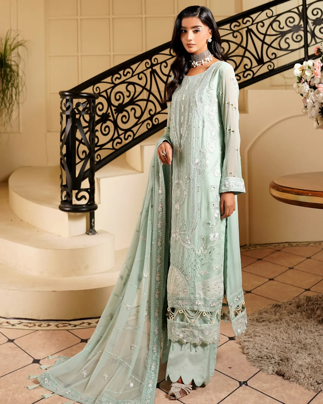 Woman in a light green traditional outfit standing in a decorative interior setting.