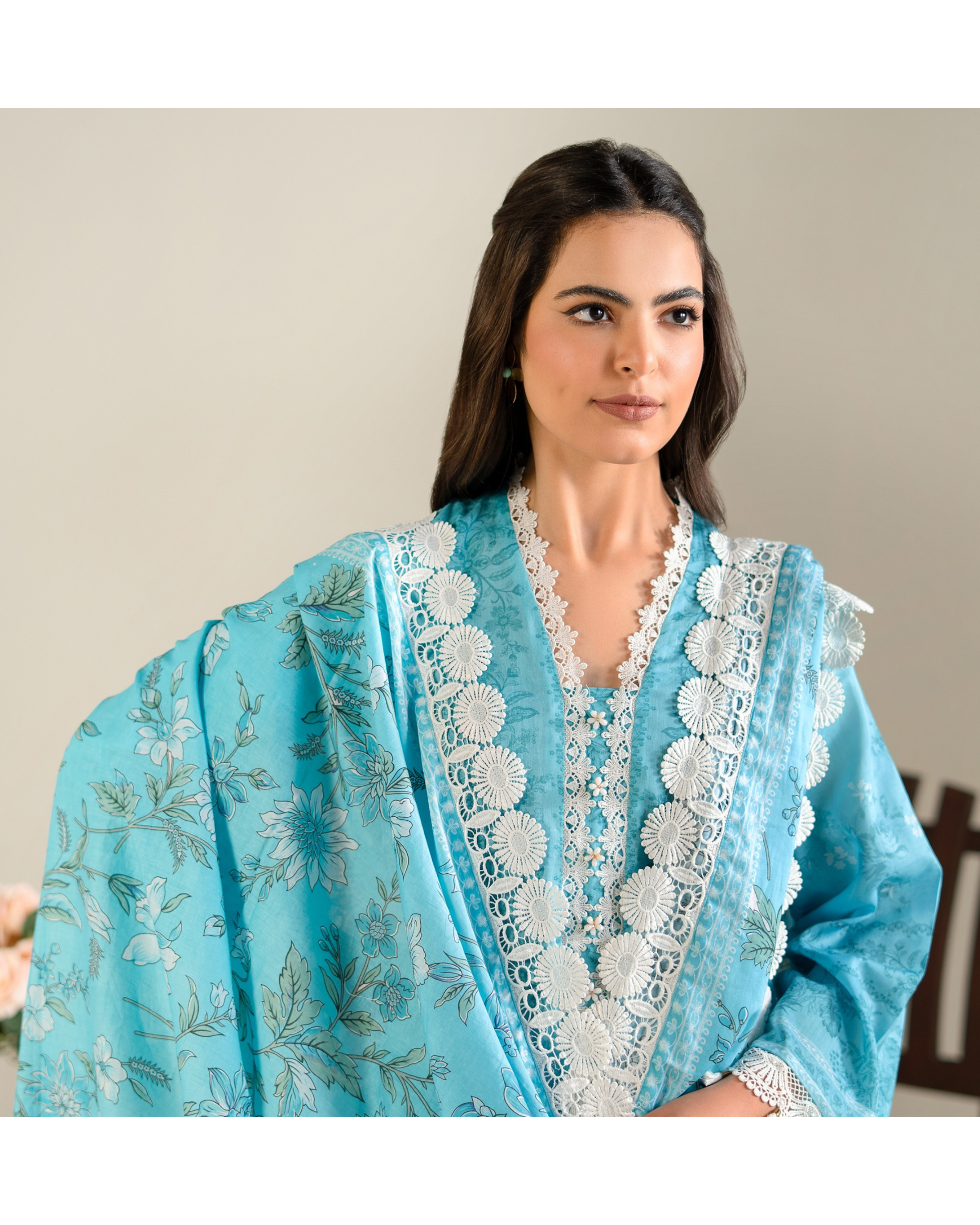 Woman wearing a light blue embroidered traditional outfit with a neutral background