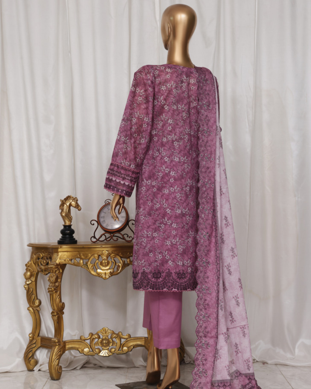 Purple embroidered outfit with pink dupatta on a mannequin against a white curtain background