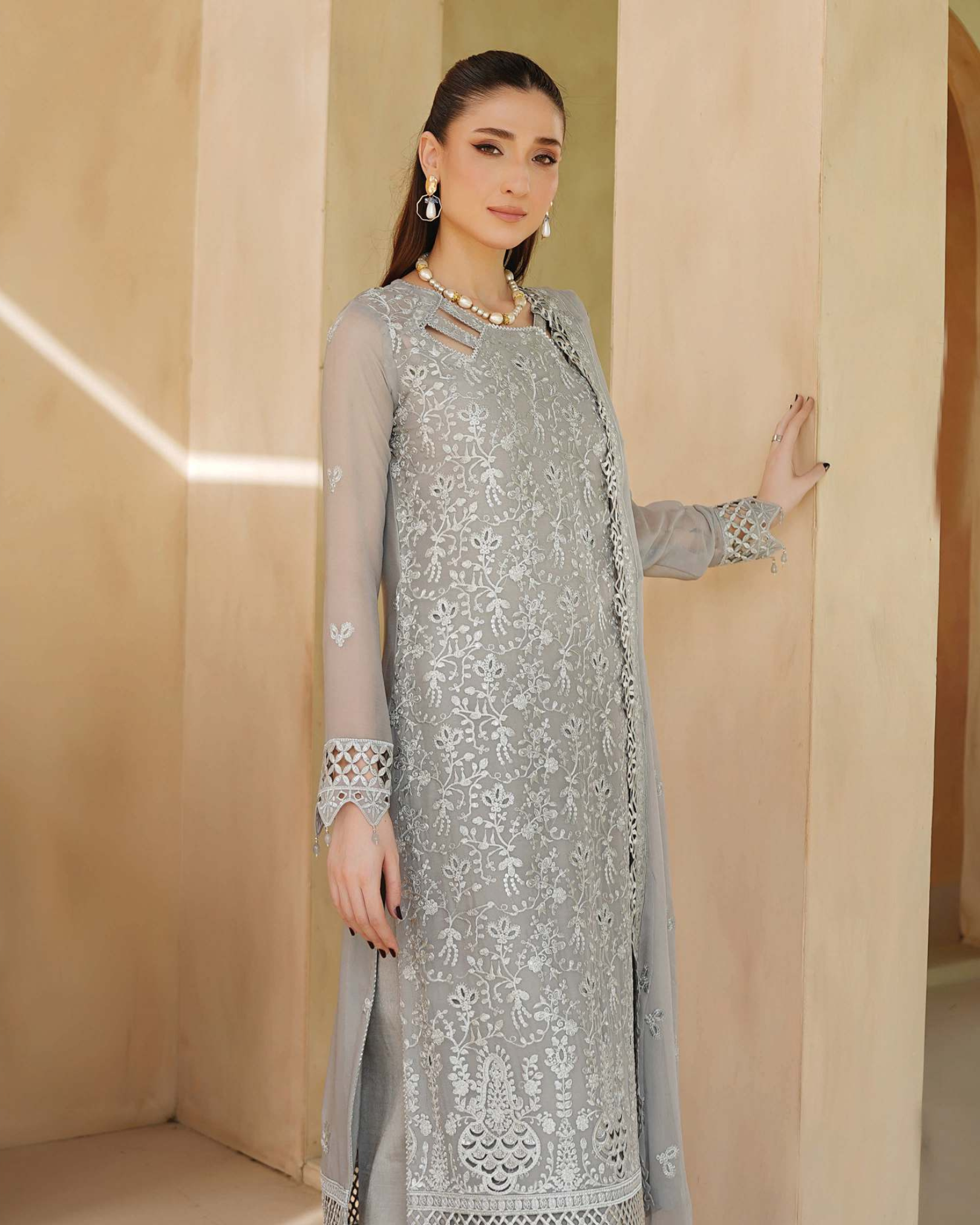 Woman wearing a light gray embroidered outfit against a beige background