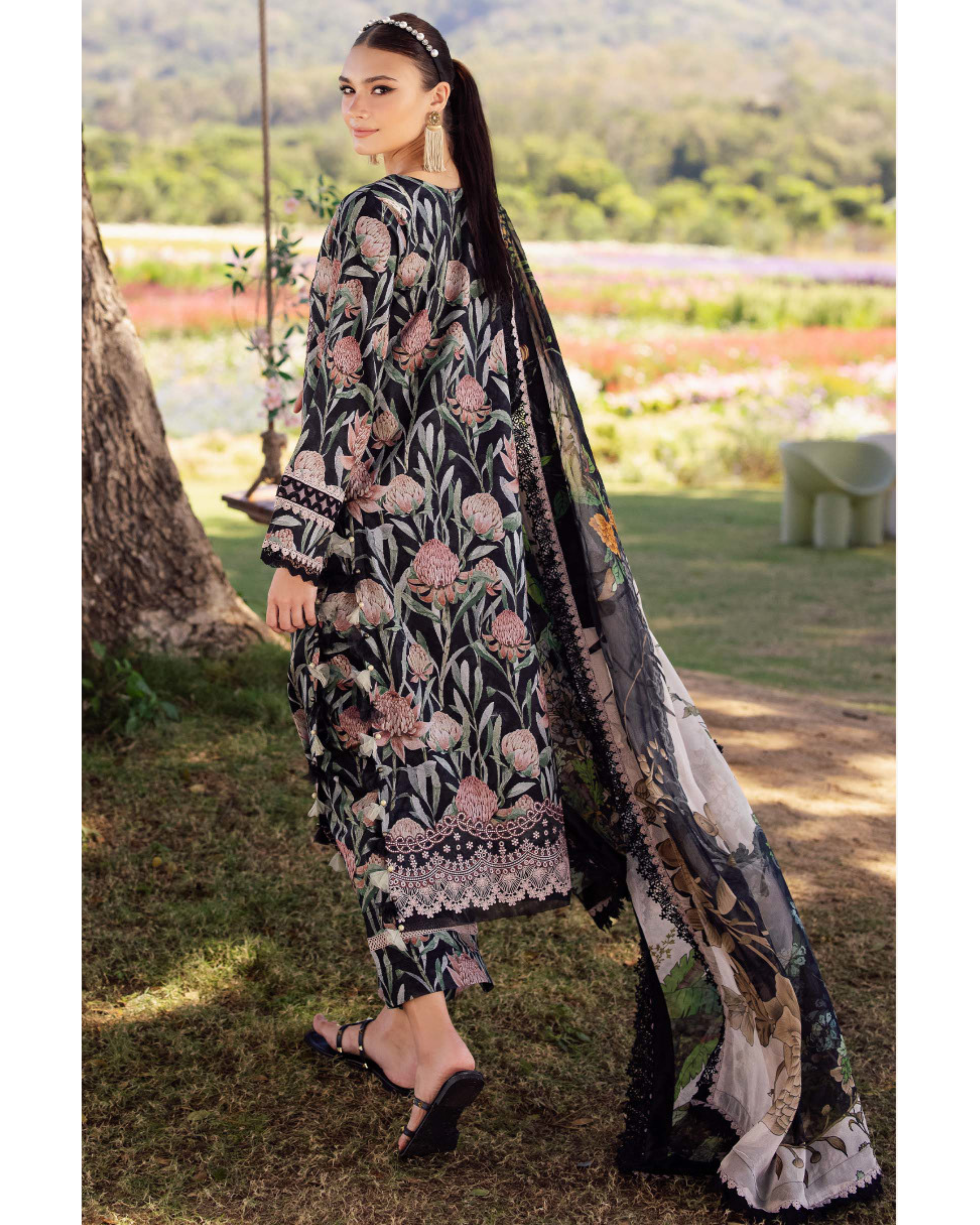 Woman in a floral embroidered outfit with a long scarf in an outdoor setting.