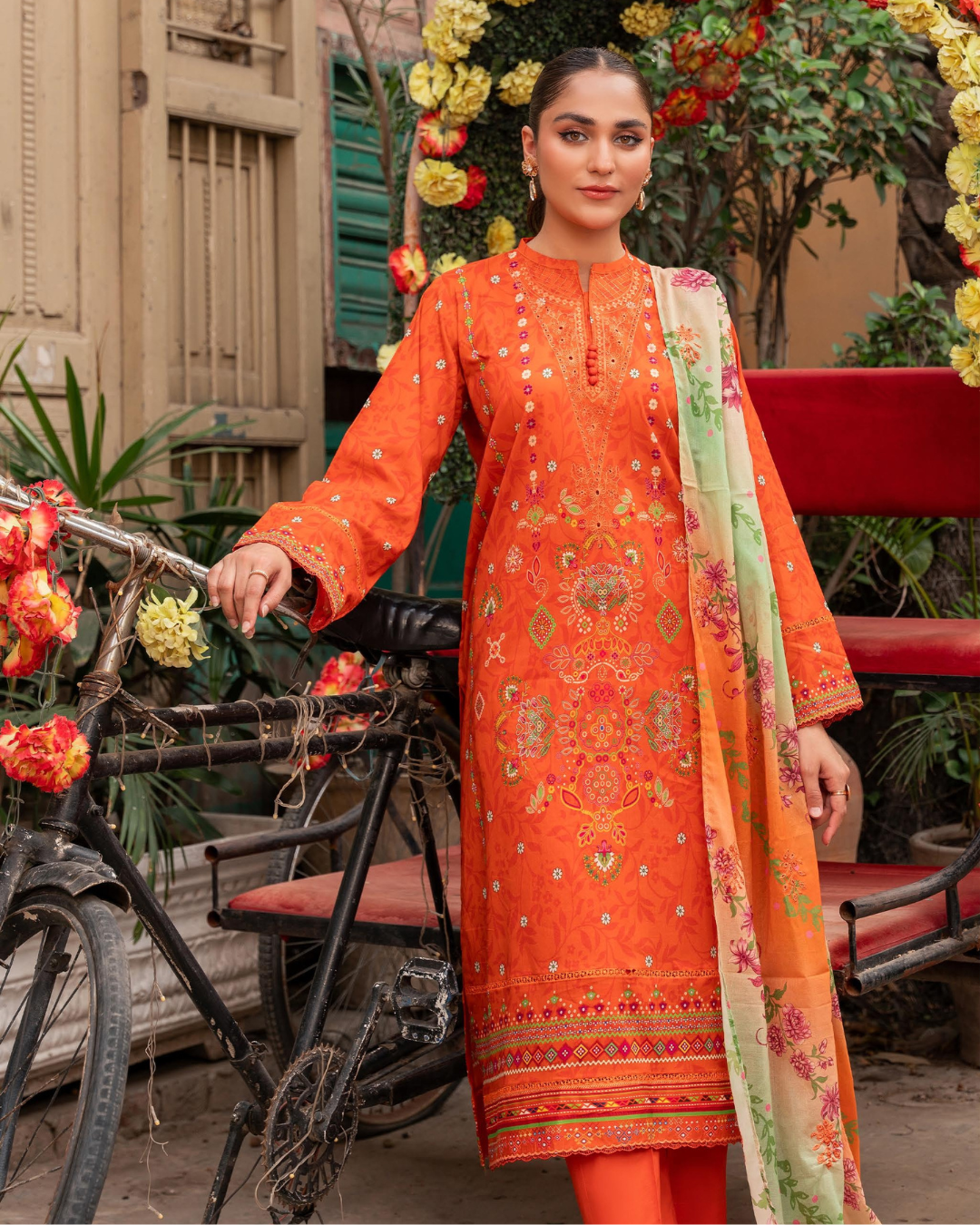 Woman in an orange embroidered outfit standing next to a bicycle with floral decorations.