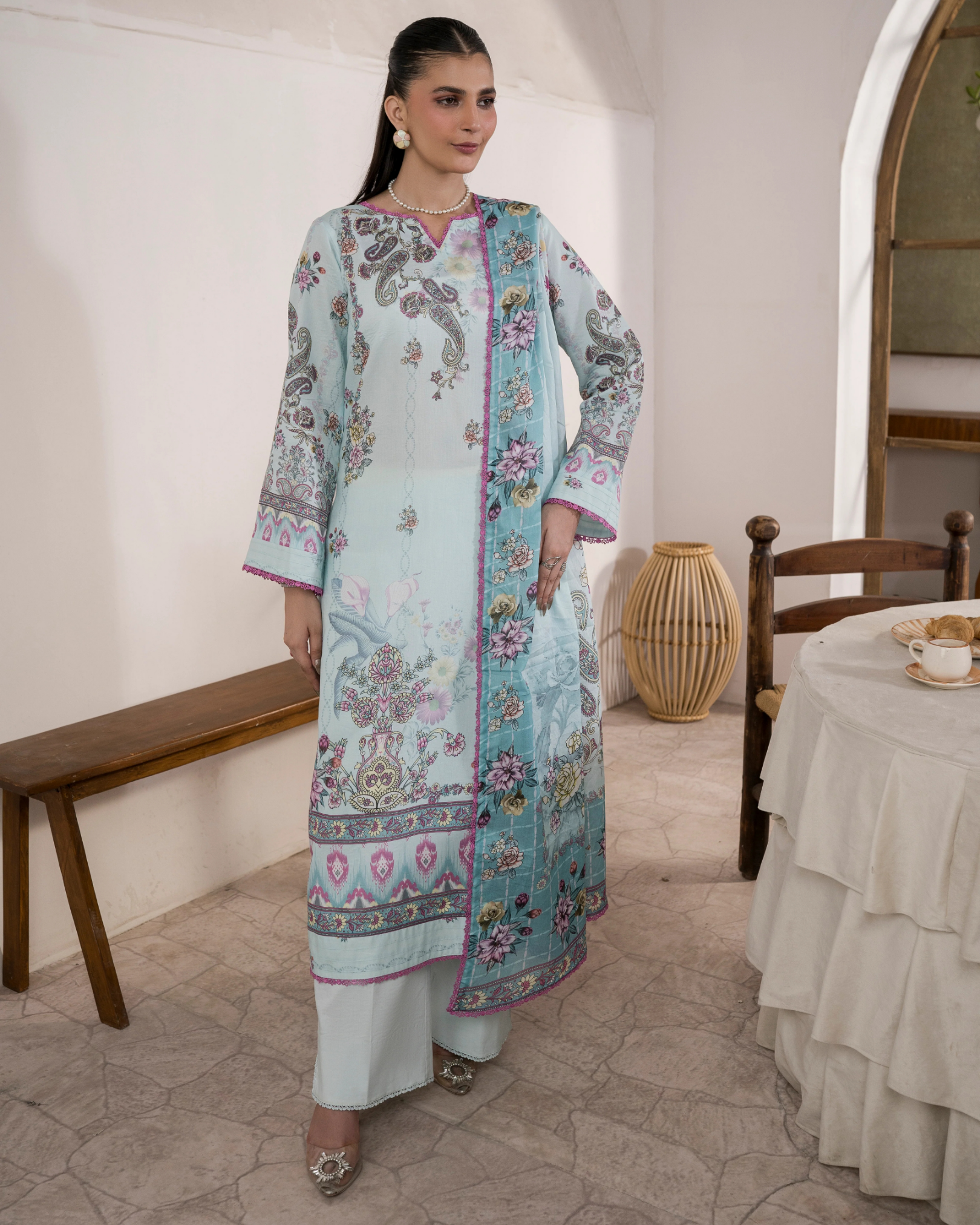 Woman in a light blue and white traditional outfit with floral patterns in a room.