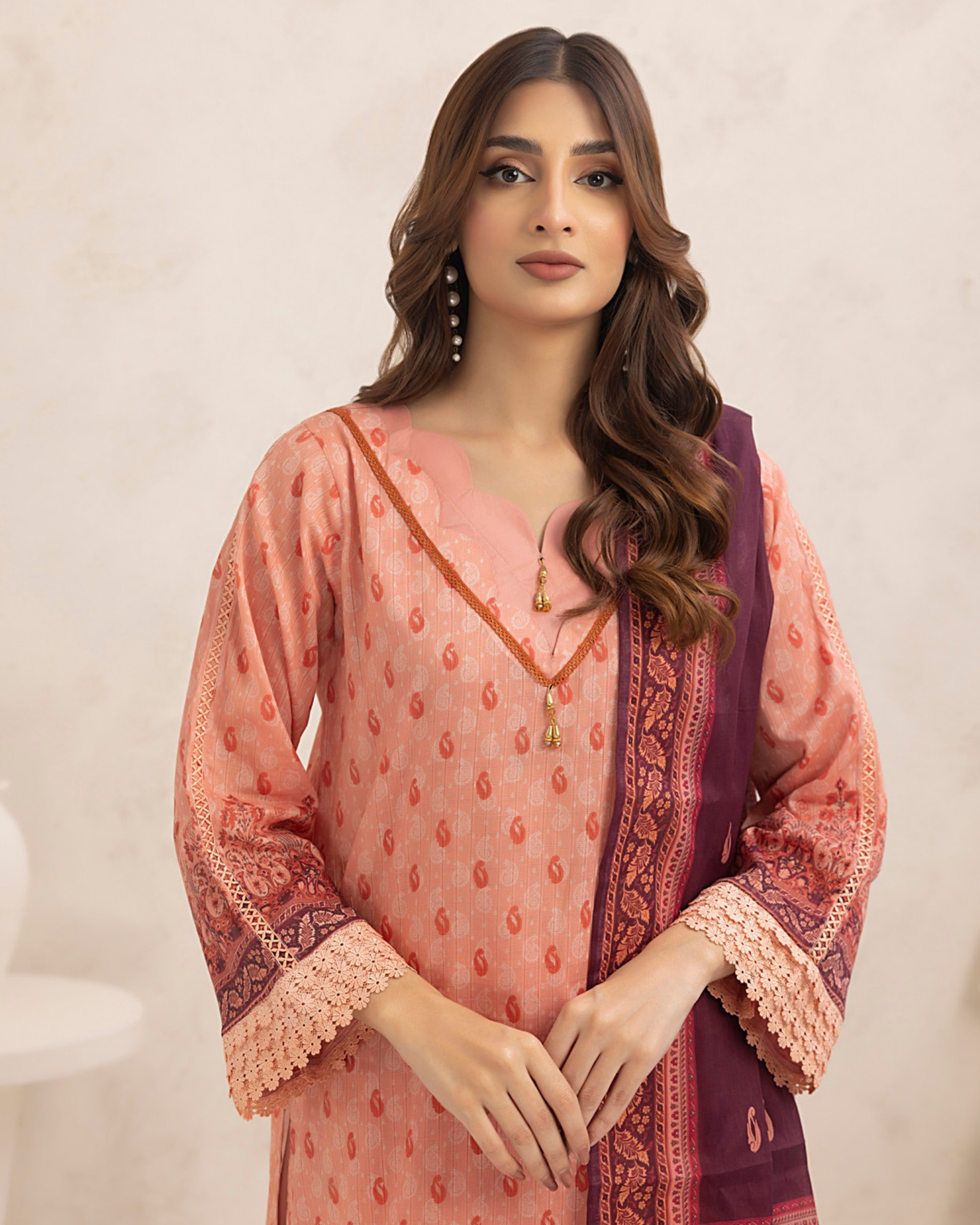 Woman wearing a pink and purple traditional outfit with intricate patterns on a beige background