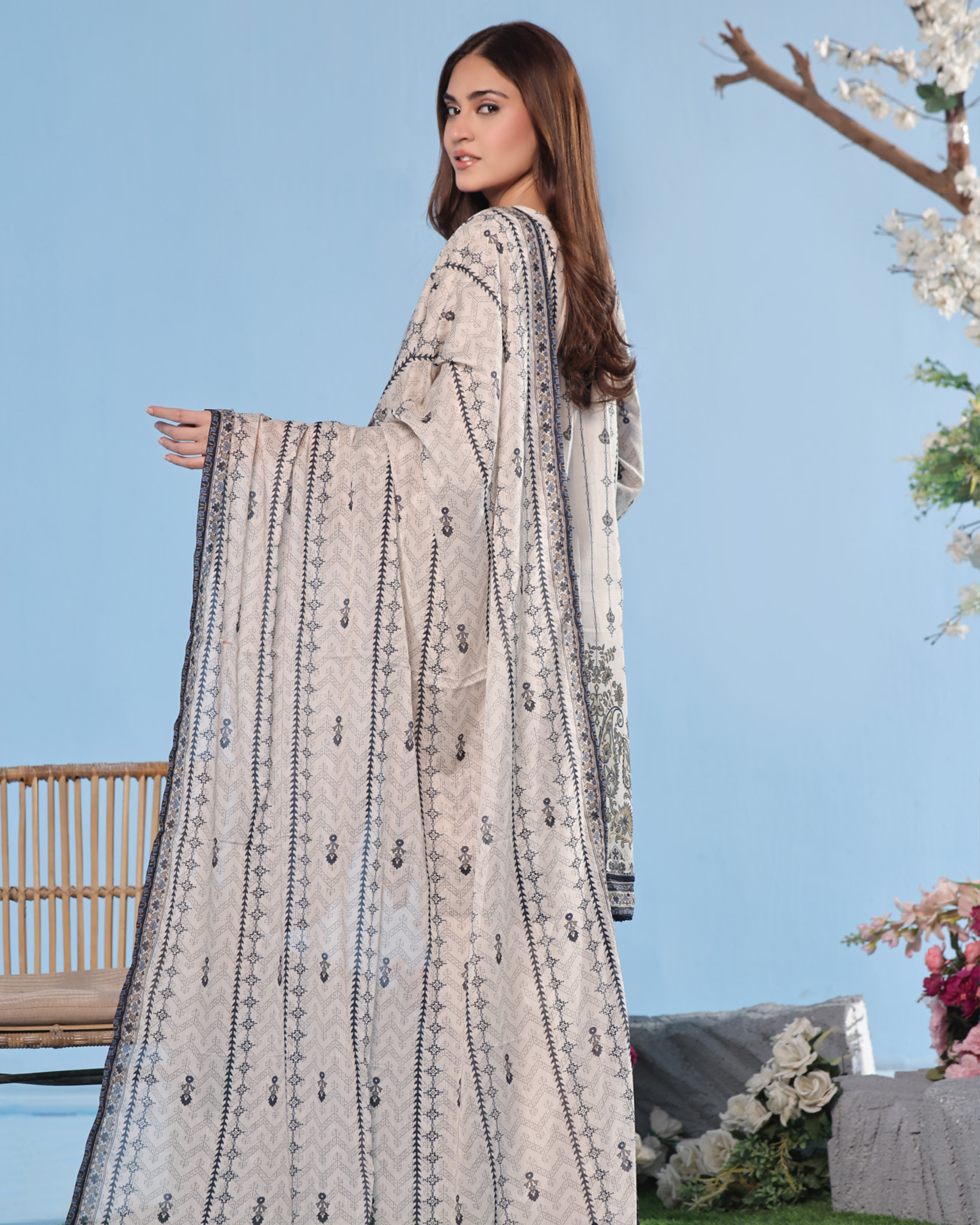 Woman wearing a long, patterned dress with a clear blue sky and outdoor setting in the background.