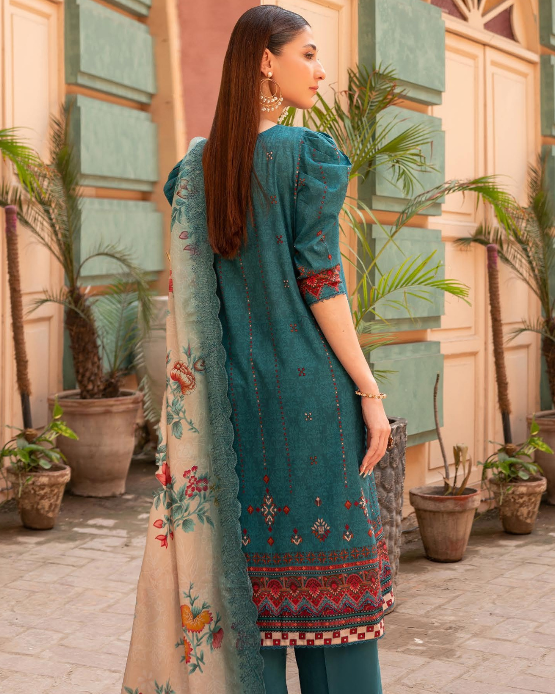 Woman wearing a teal embroidered outfit with a floral dupatta in an outdoor setting.