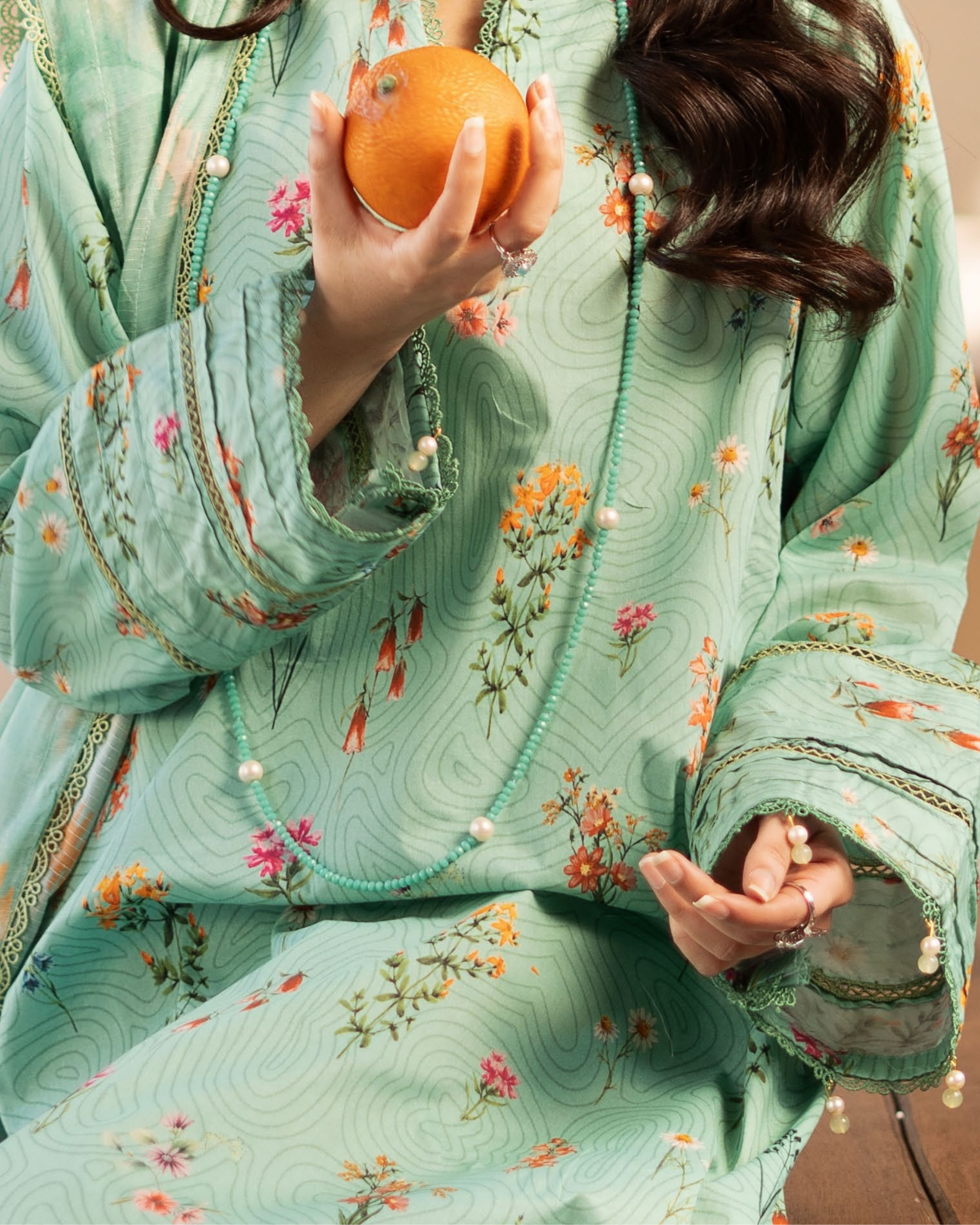 Person wearing a light green floral dress holding an orange.