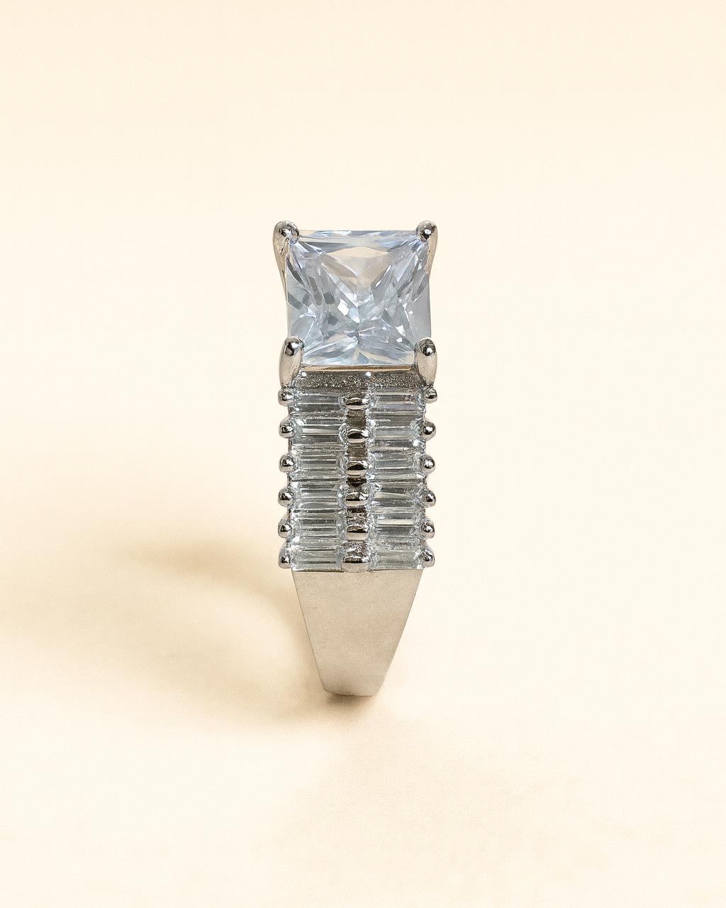 Silver ring with a large central gemstone and smaller baguette-cut stones on a beige background