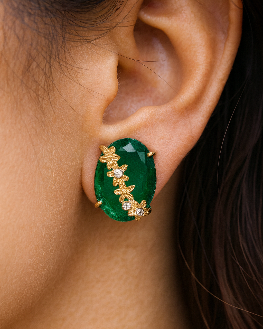 Close-up of an ear wearing a green and gold earring.