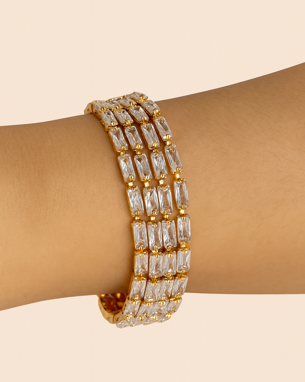 Gold bracelet with clear stones on a wrist against a beige background