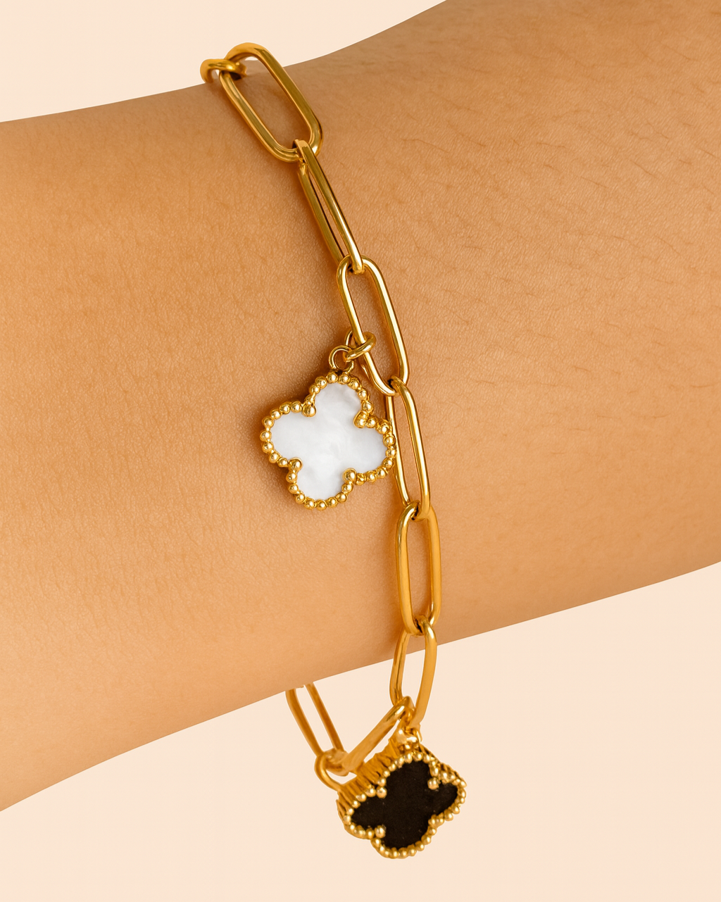 Gold chain bracelet with clover charms on a wrist against a beige background