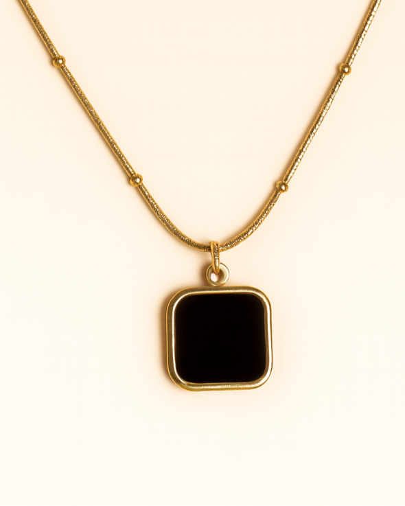 Gold necklace with a black square pendant on a beige background