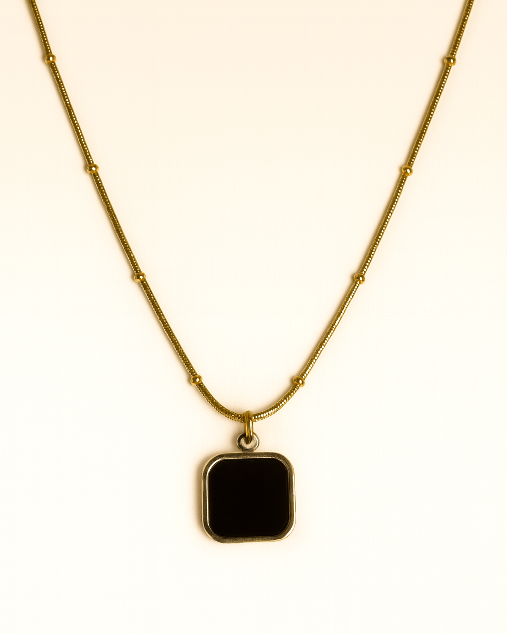 Gold necklace with a black square pendant on a white background