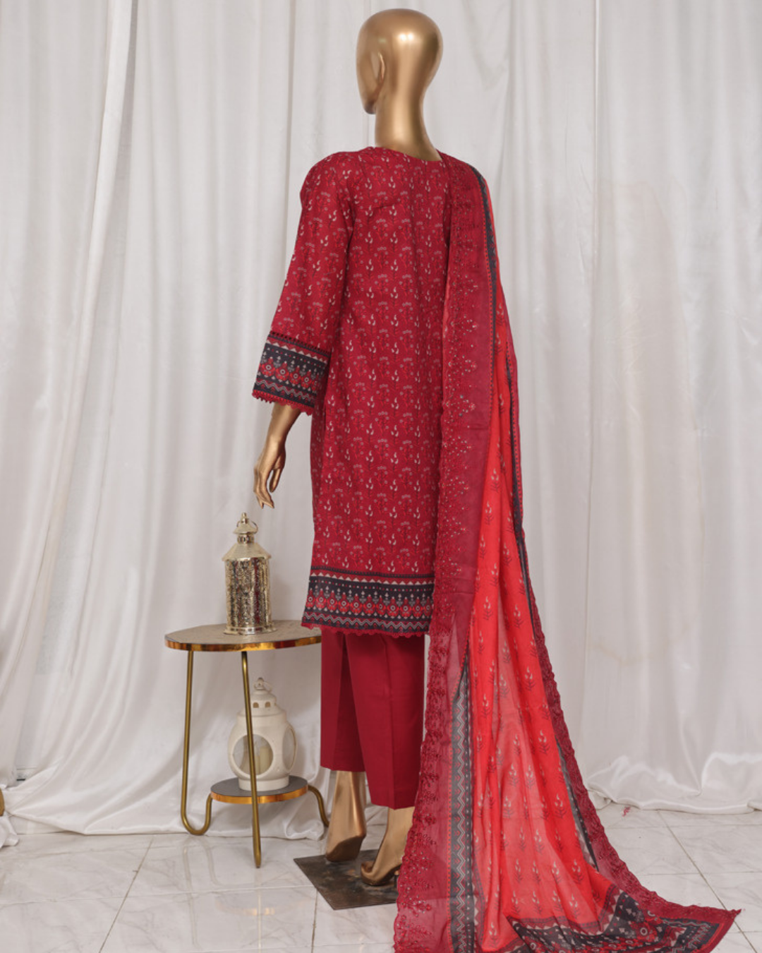 Red patterned outfit with a dupatta on a mannequin against a white curtain background