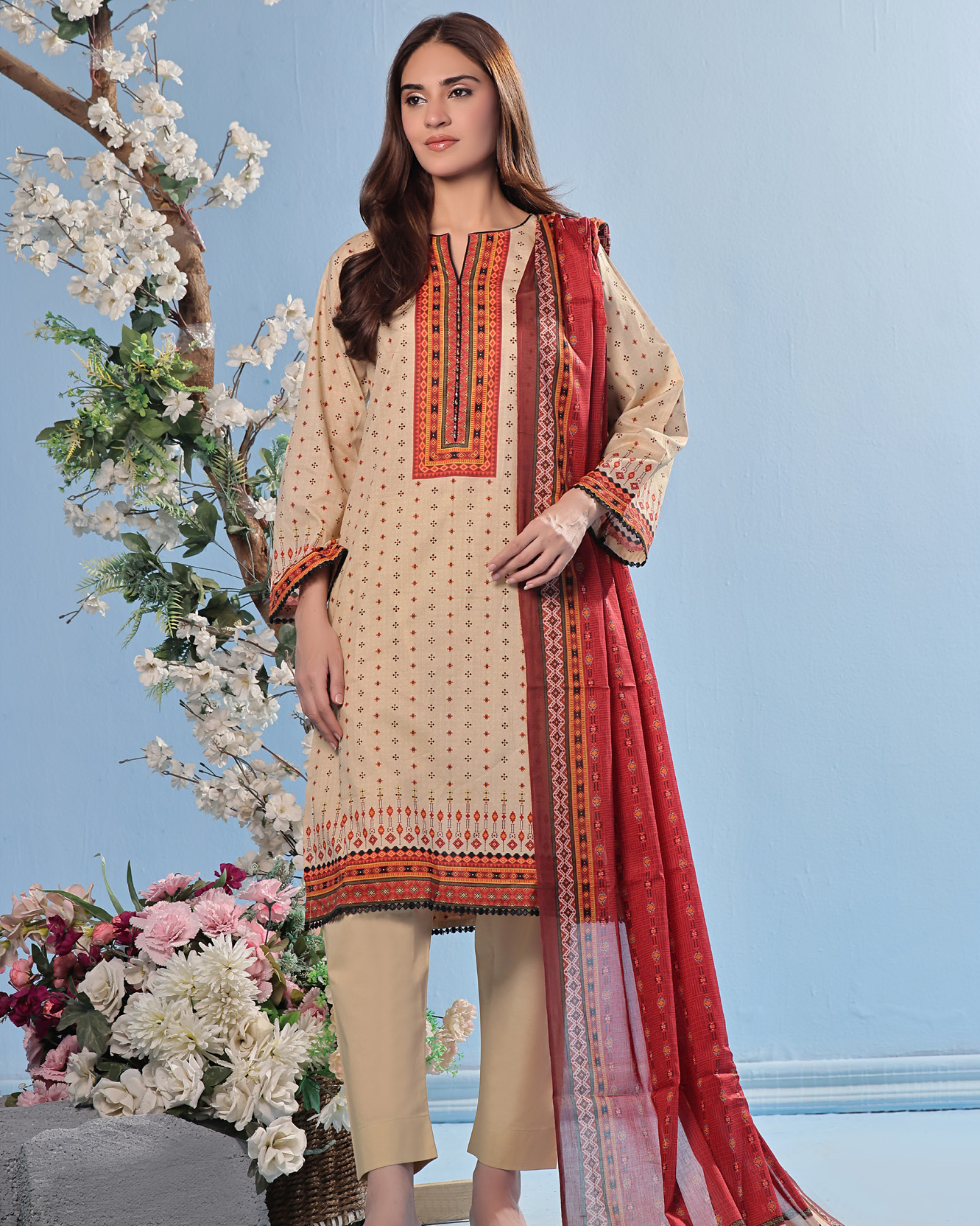 Woman in a traditional outfit with a red dupatta against a light blue background