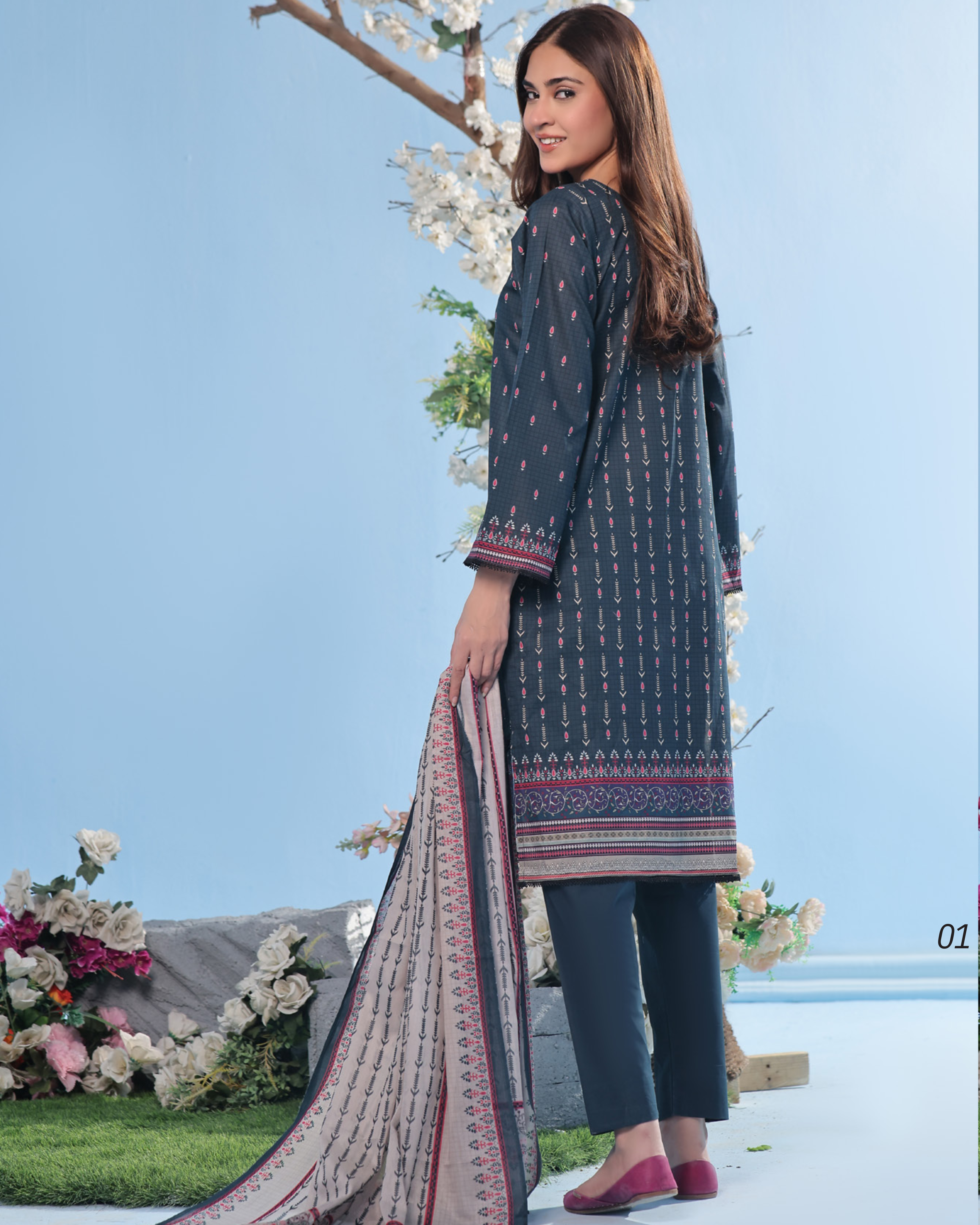 Woman wearing a dark blue traditional outfit with a patterned dupatta against a light blue sky.