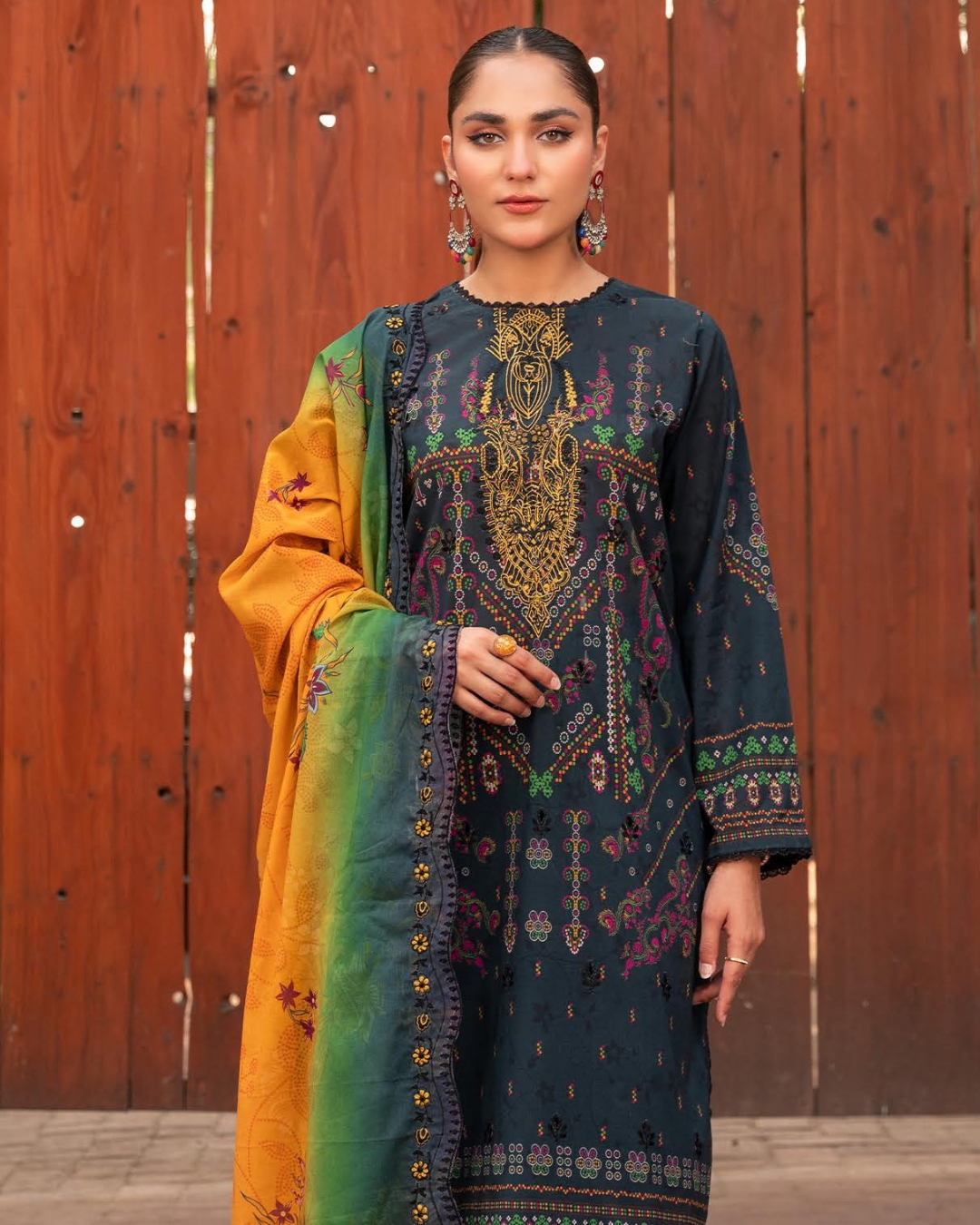 Woman wearing a traditional embroidered outfit with a colorful dupatta against a wooden background