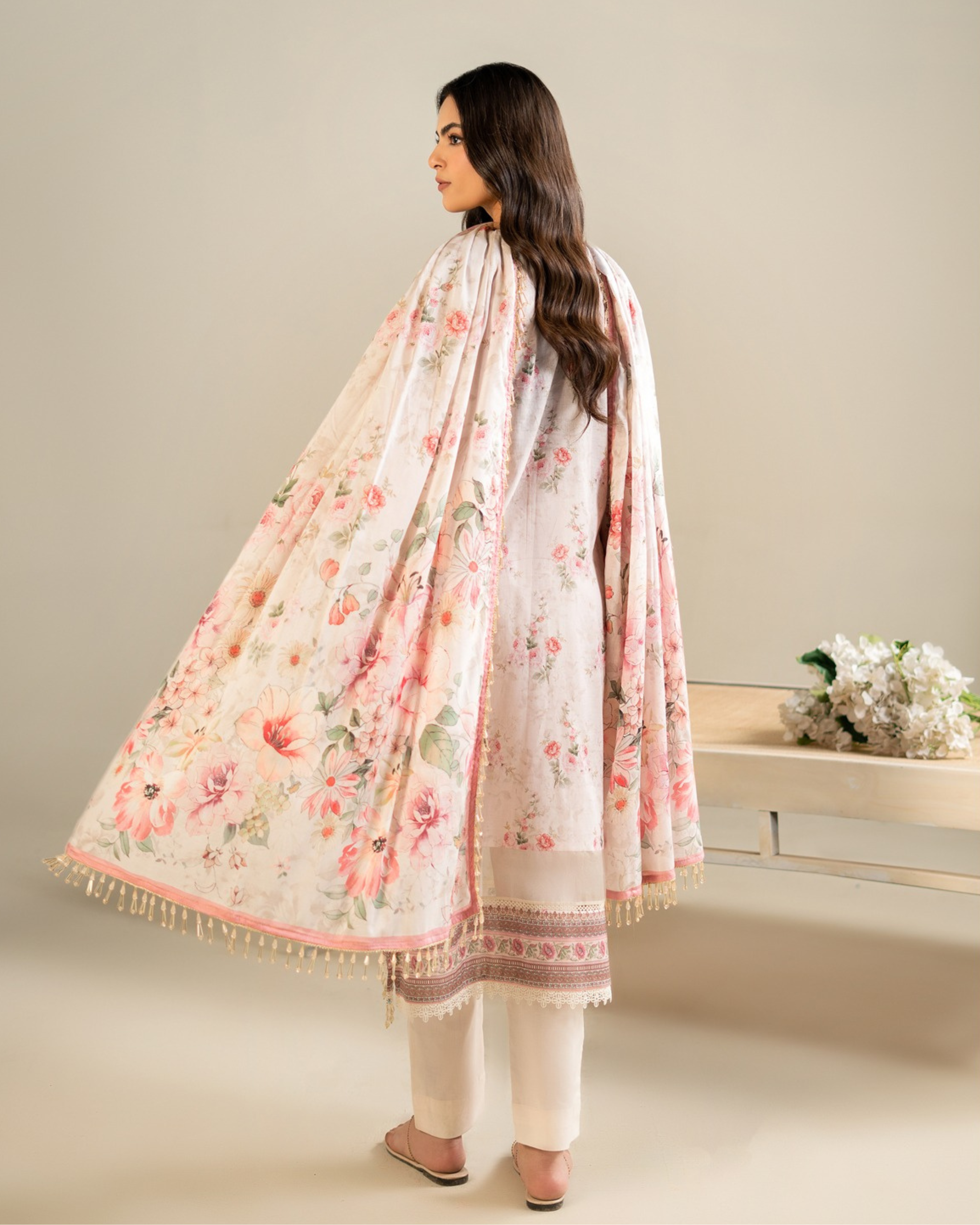 Woman wearing a floral dupatta and white outfit on a neutral background