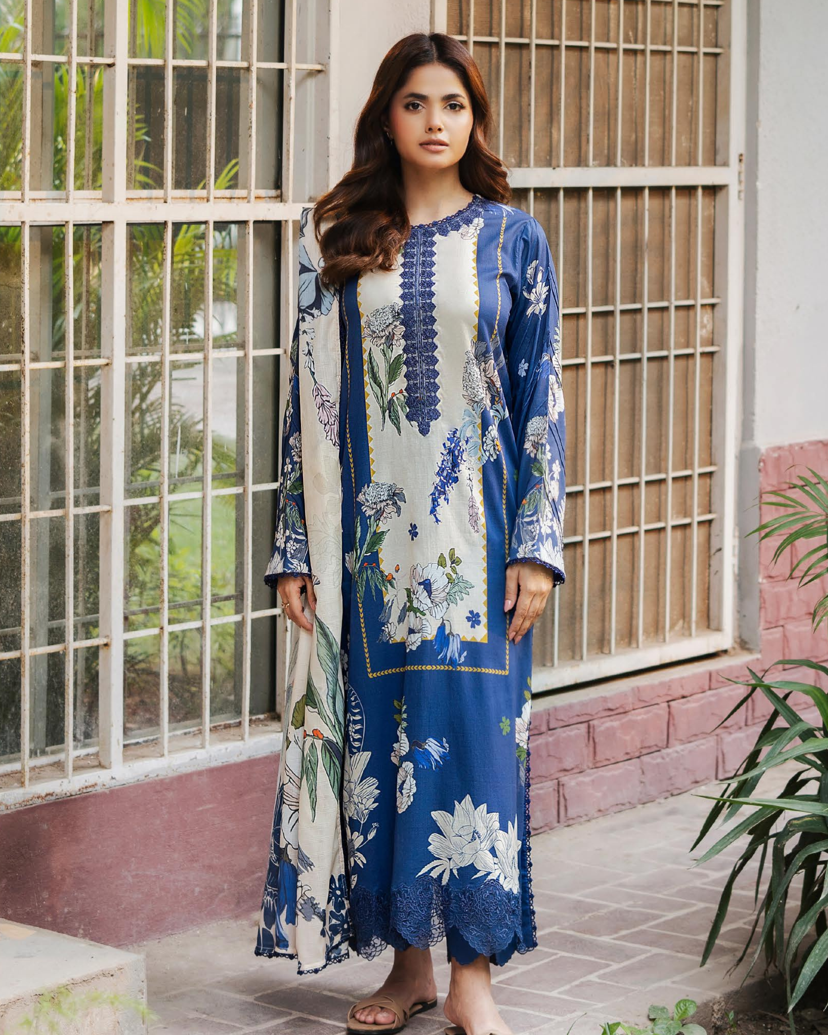 Woman wearing a blue and white floral dress standing in front of a window.