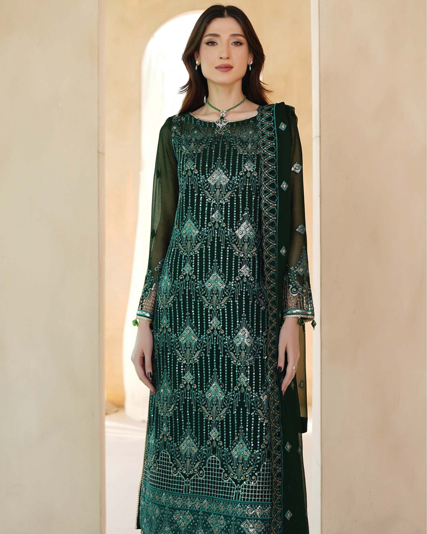Woman wearing a green embroidered traditional outfit against a beige background