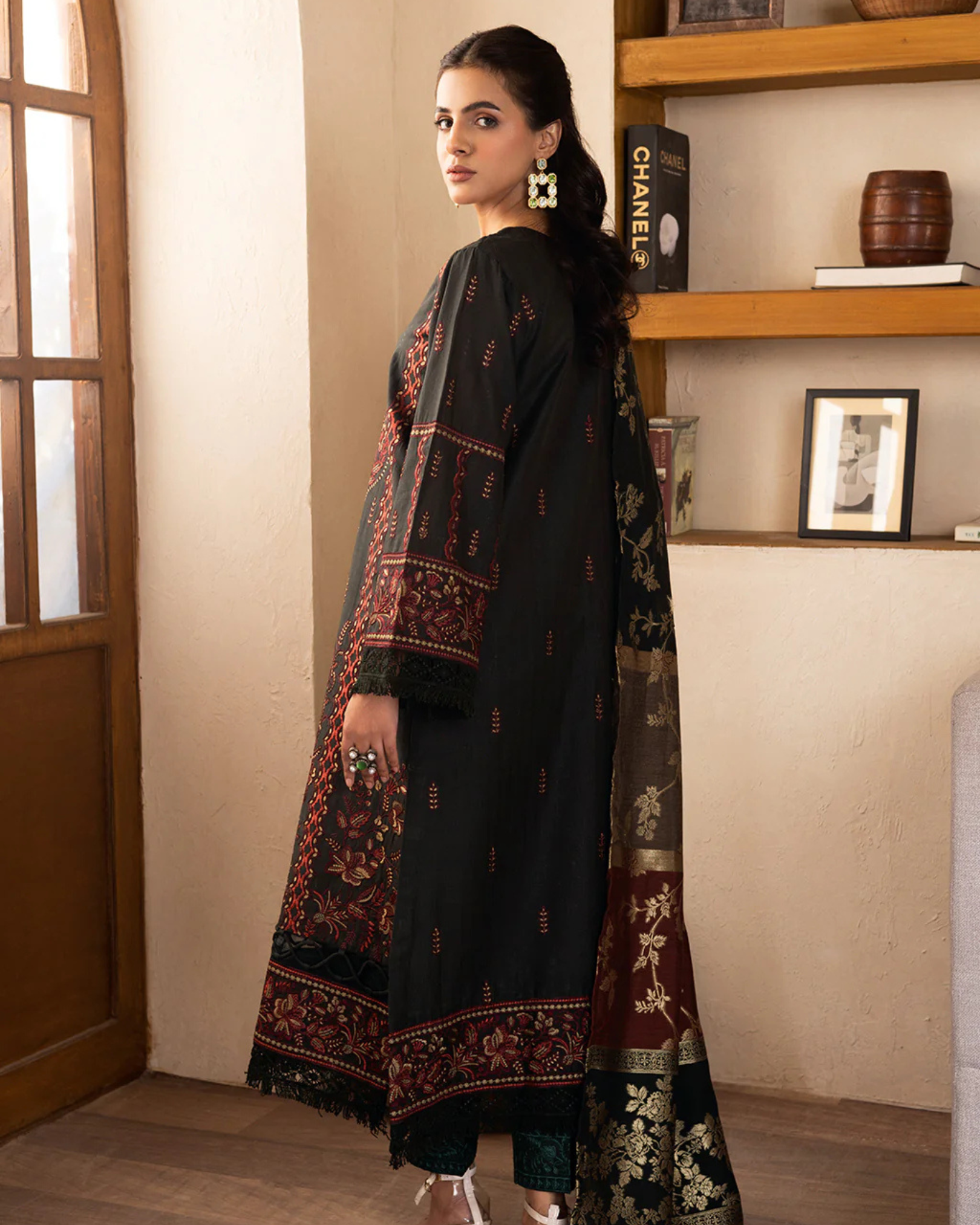 Woman wearing a black embroidered outfit in a room with a bookshelf.