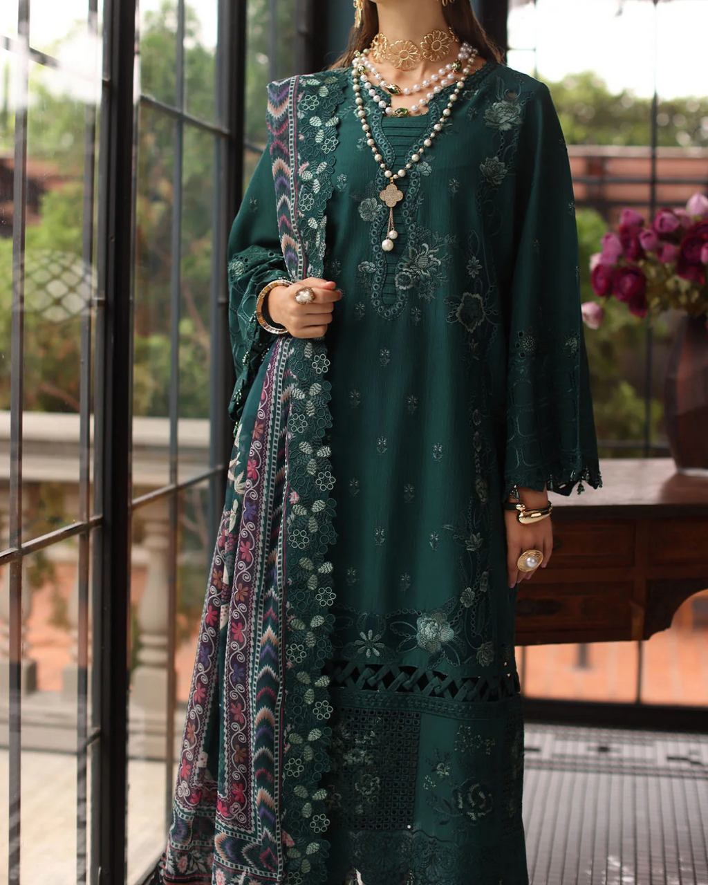 Woman wearing a dark green embroidered dress with a colorful scarf, standing indoors.