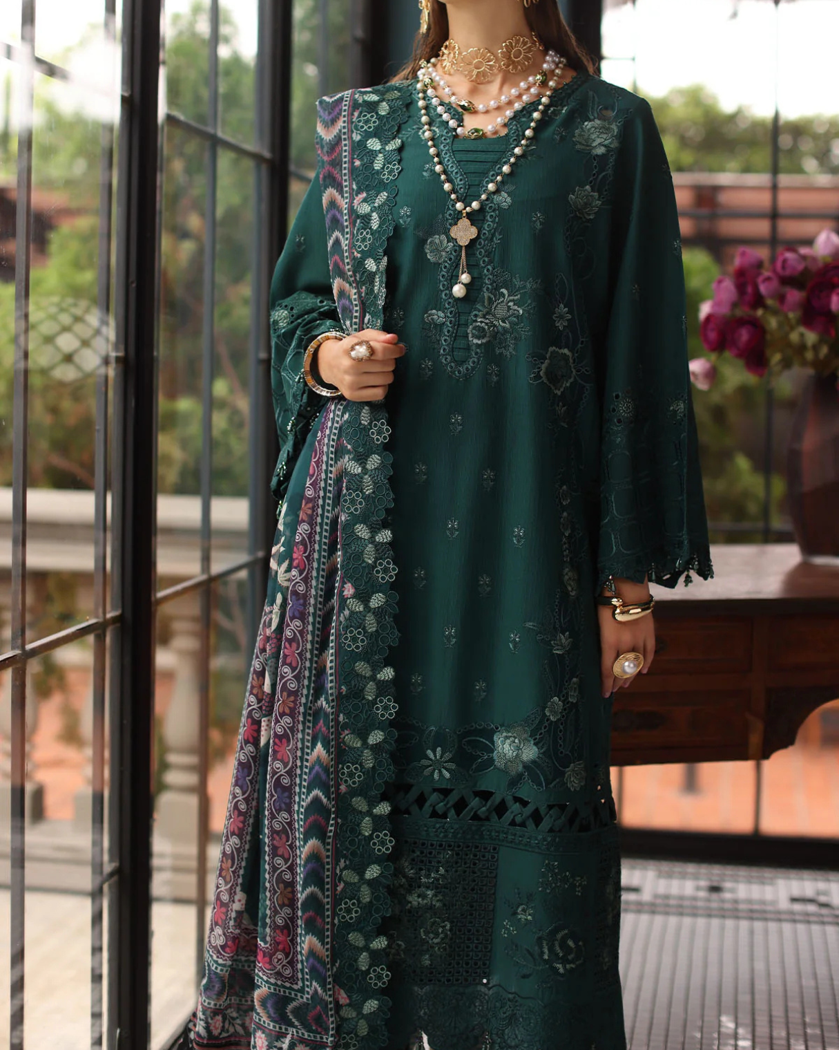 Woman wearing a dark green embroidered dress with a colorful scarf, standing indoors.
