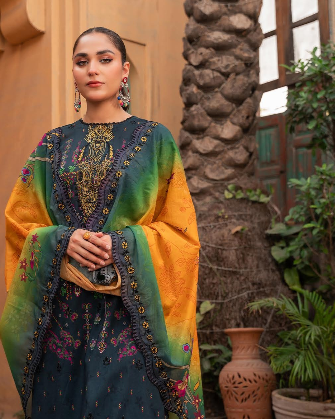 Woman wearing a colorful embroidered traditional outfit with a stone wall and plants in the background