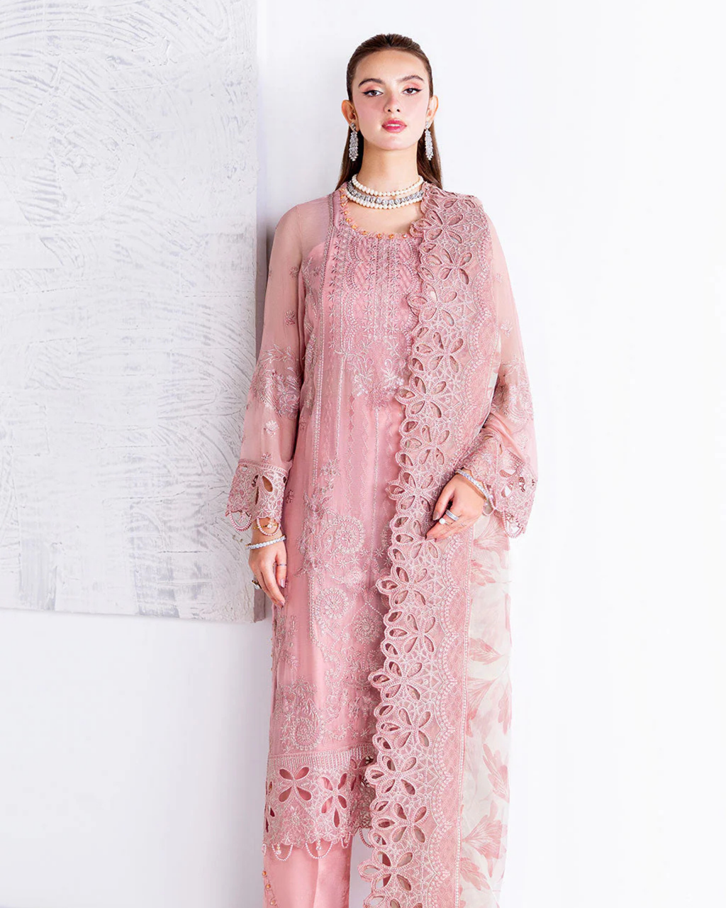 Woman wearing a pink lace outfit against a white brick wall.