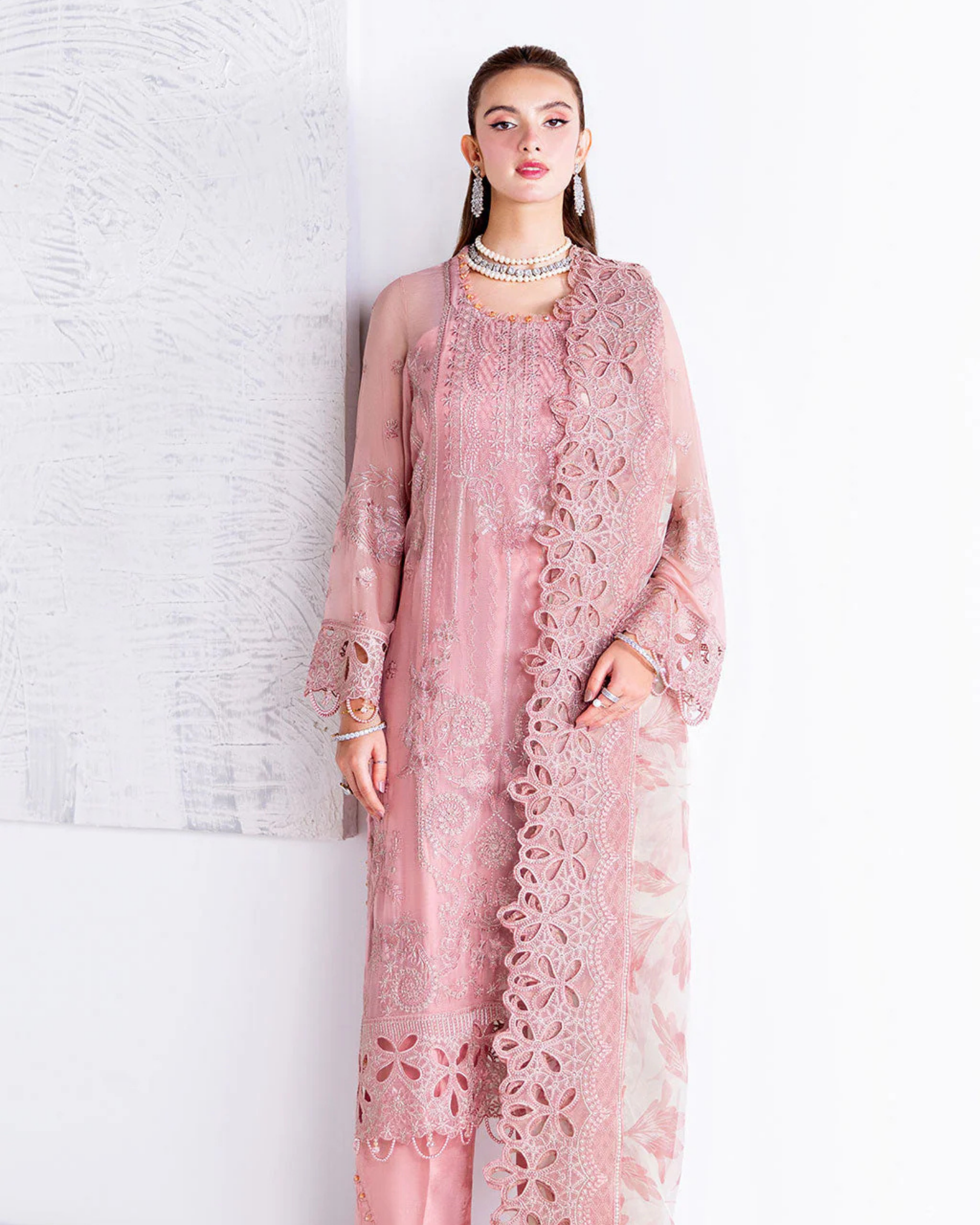 Woman wearing a pink lace outfit against a white brick wall.