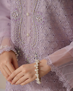 Close-up of a person wearing a pearl bracelet with a detailed embroidered garment in the background.