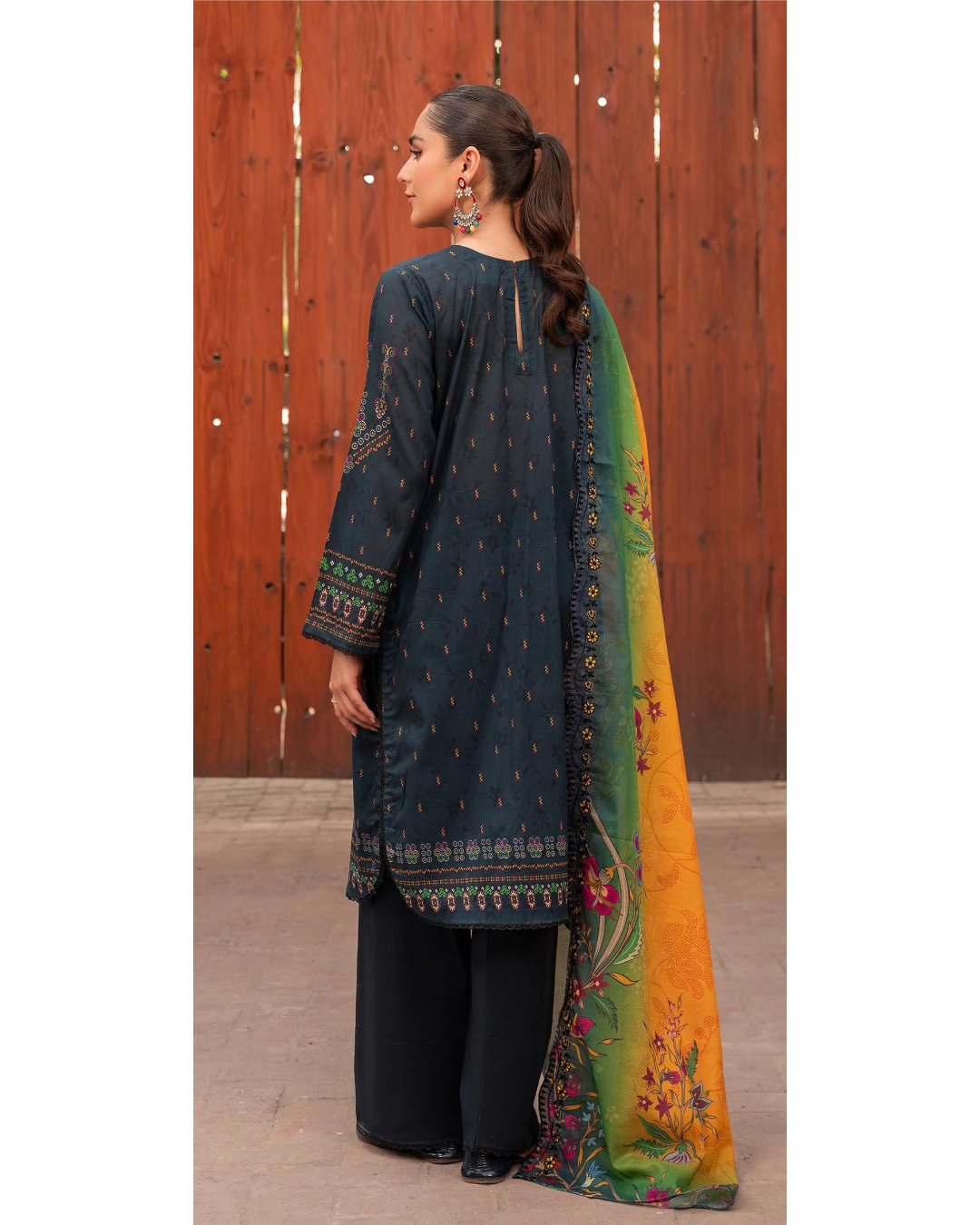 Woman wearing a dark blue embroidered shirt with black pants and a colorful scarf against a wooden background