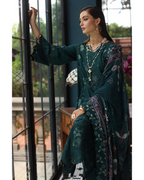 Woman in a dark green traditional outfit with floral patterns, sitting by a window.