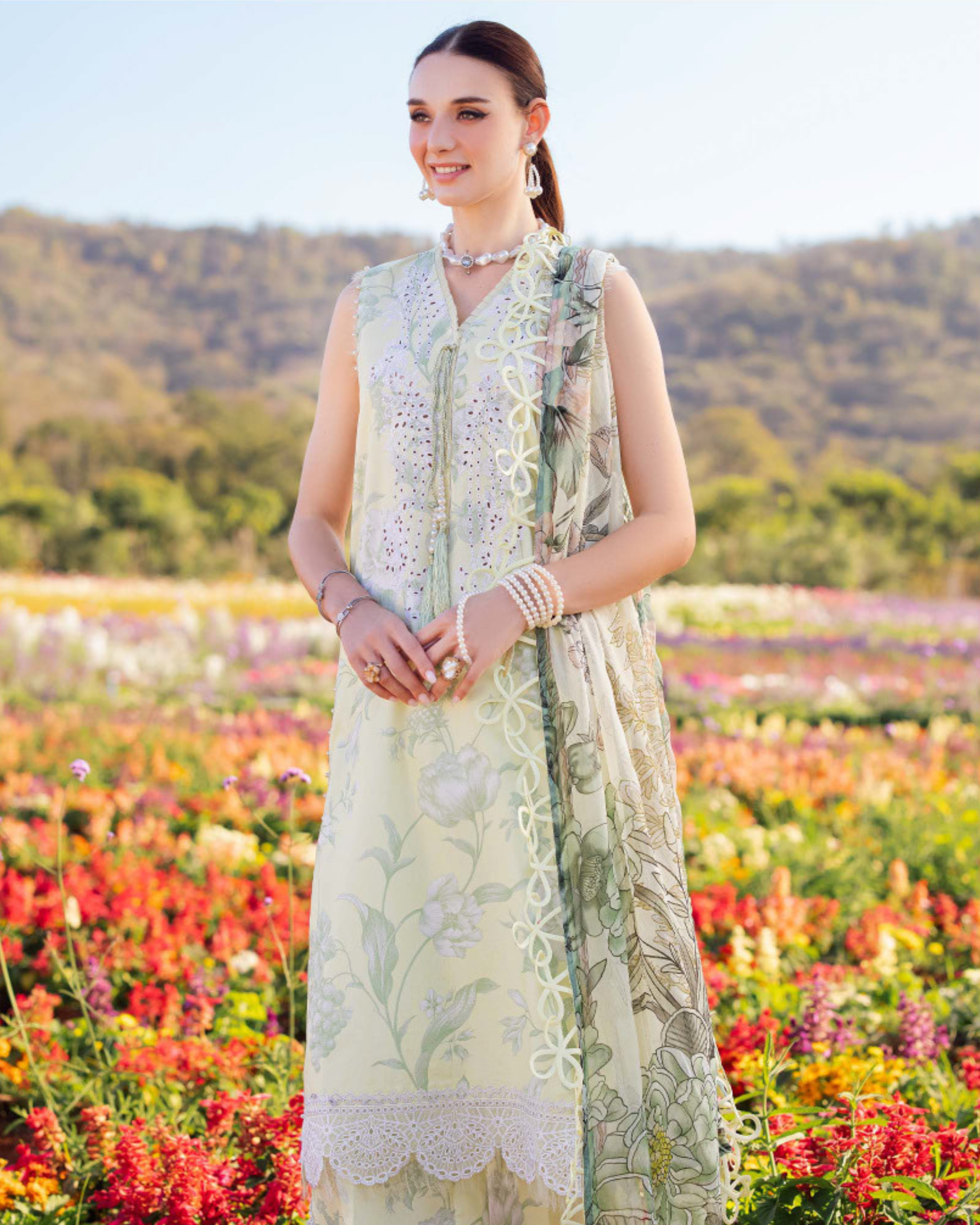 Woman in a floral dress standing in a field of colorful flowers with mountains in the background