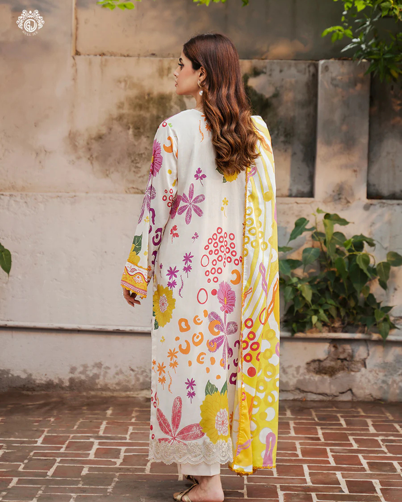 Woman wearing a floral dress with a yellow dupatta in an outdoor setting.