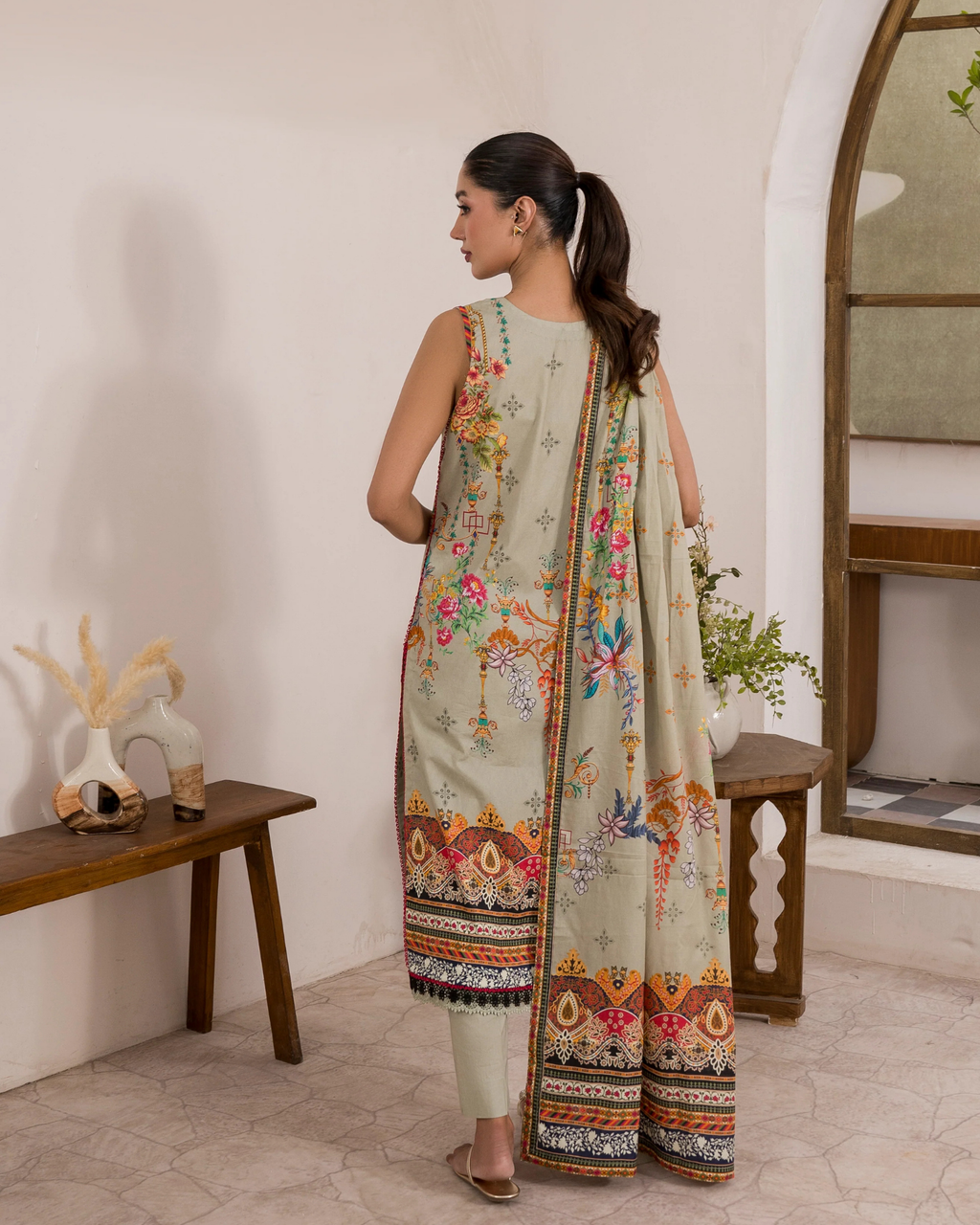Woman in a traditional outfit with floral patterns in a room setting.
