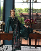 Woman in a dark green embroidered dress sitting on a wooden desk with a decorative background.