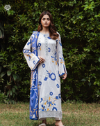 Woman wearing a blue and white floral outfit standing in front of green foliage.