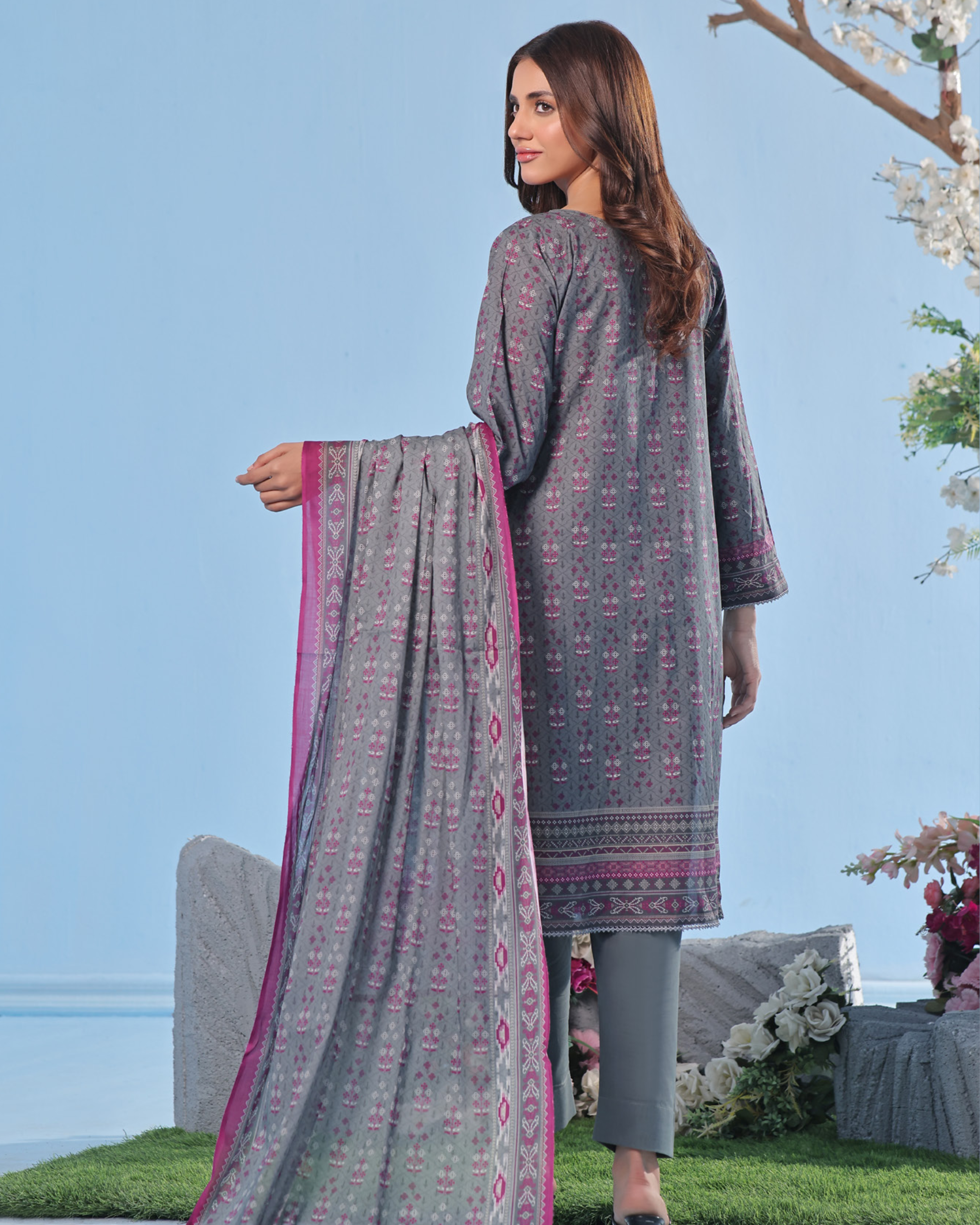 Woman wearing a gray patterned outfit with a matching dupatta, standing outdoors with a clear blue sky.