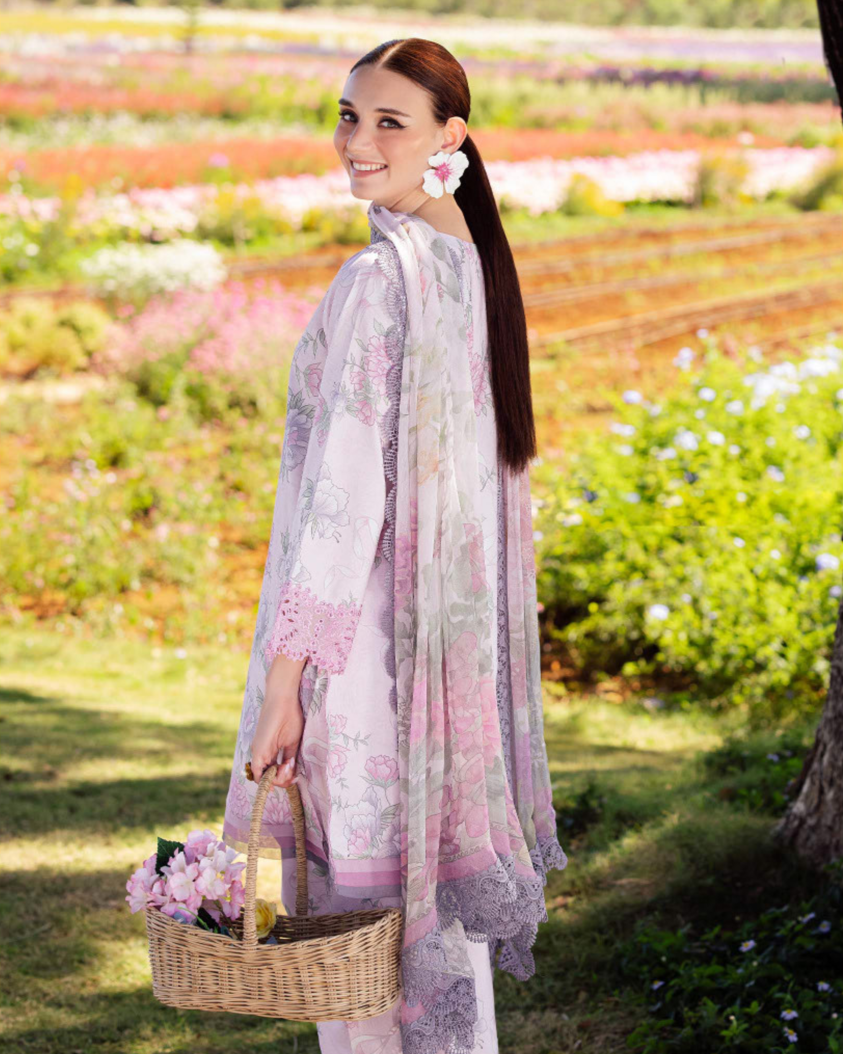 Woman in a floral dress standing in a garden holding a picnic basket.