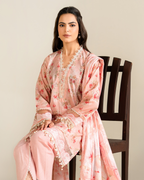 Woman in a pink traditional outfit with floral patterns sitting on a wooden chair.