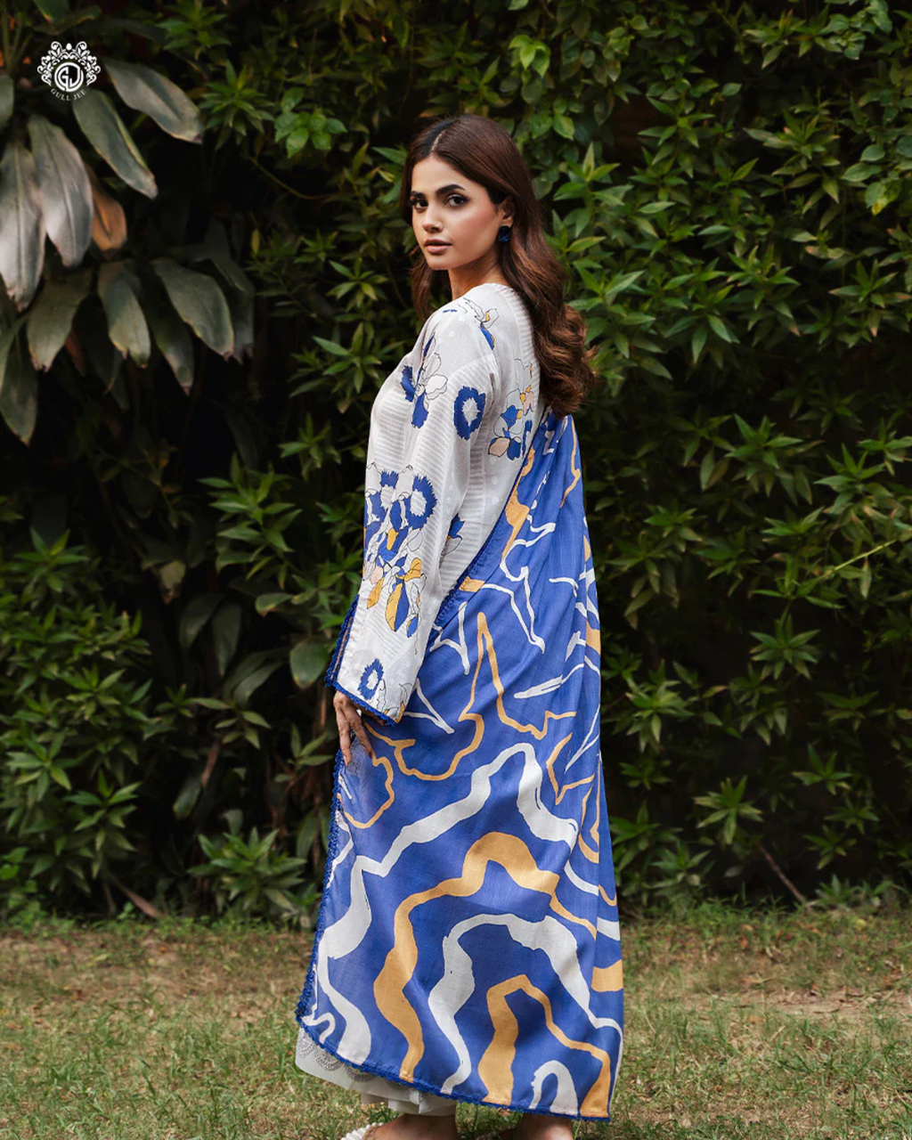 Woman wearing a blue and white patterned dress with a white cardigan in an outdoor setting.