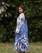 Woman wearing a blue and white patterned dress with a white cardigan in an outdoor setting.