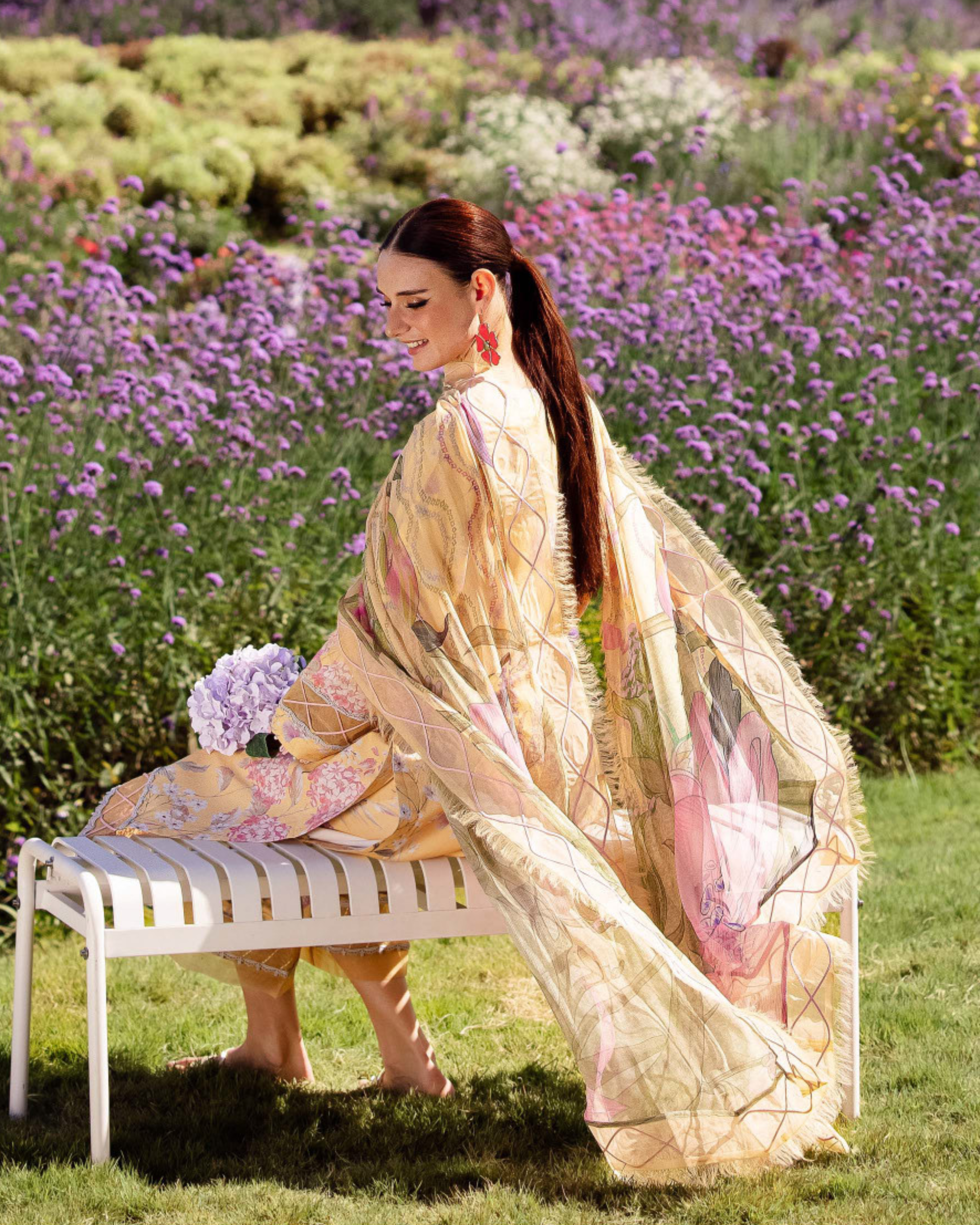 Woman in a floral dress sitting on a bench in a field of flowers