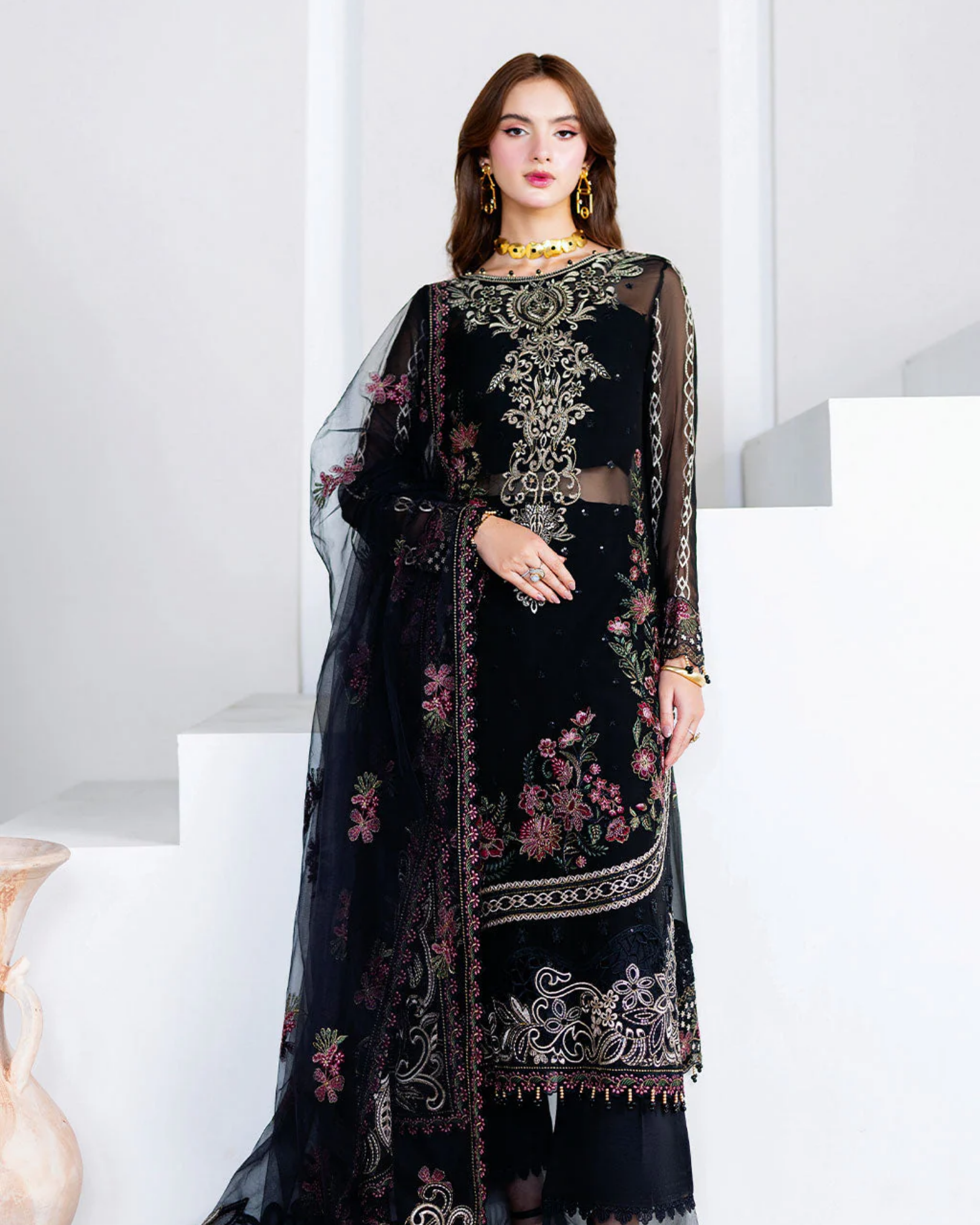 Woman wearing a black embroidered traditional outfit with a sheer overlay on a white background