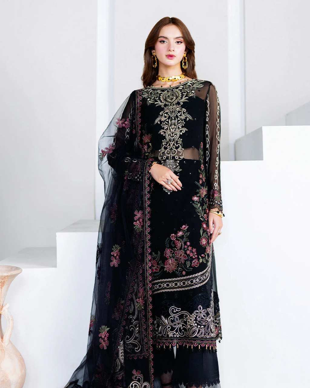 Woman wearing a black embroidered traditional outfit with a sheer overlay on a white background