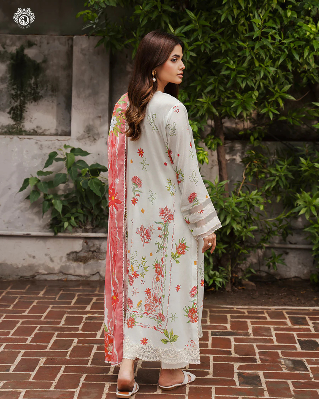 Woman wearing a floral embroidered outfit standing outdoors with greenery in the background