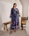Woman wearing a long, dark blue dress with floral patterns in a room with white walls and wooden furniture.