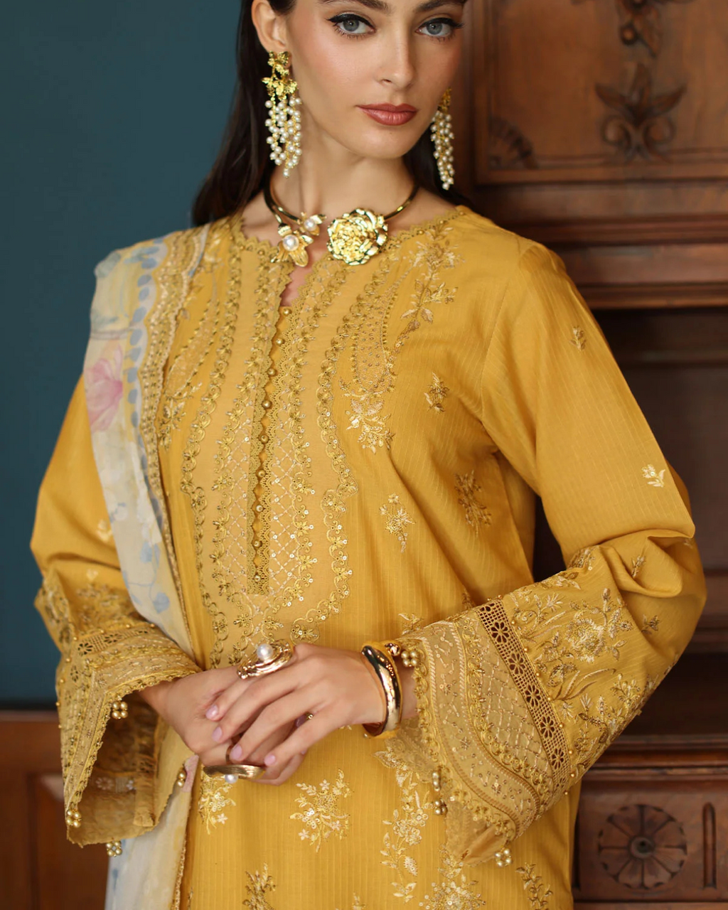 Woman wearing a mustard yellow embroidered outfit with jewelry against a wooden background